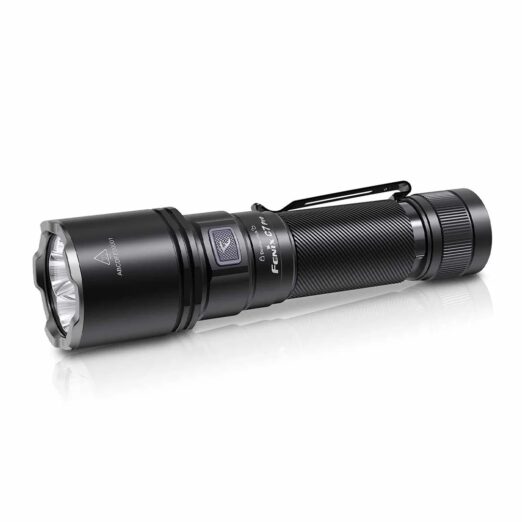 Black tactical flashlight with textured grip and metal clip, lying on a white reflective surface.