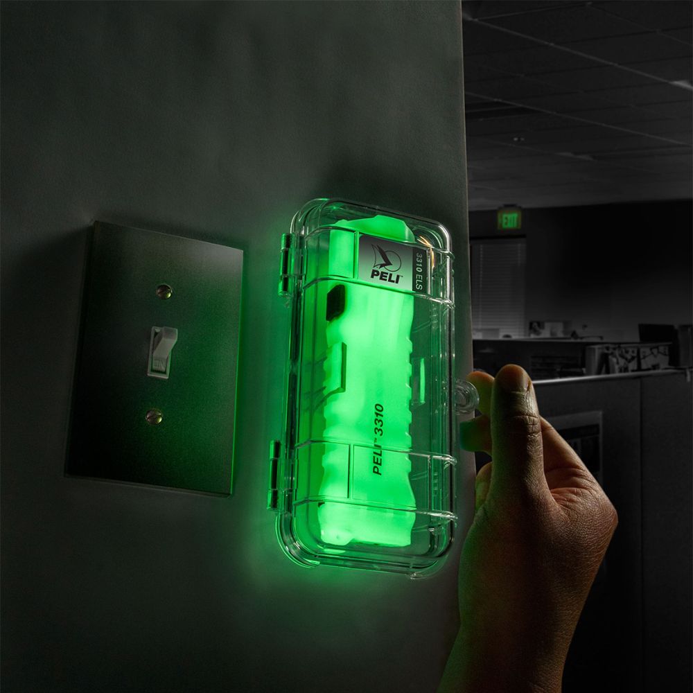 Hand turning a bright green-lit safety device in a clear case mounted on a wall beside a switch.