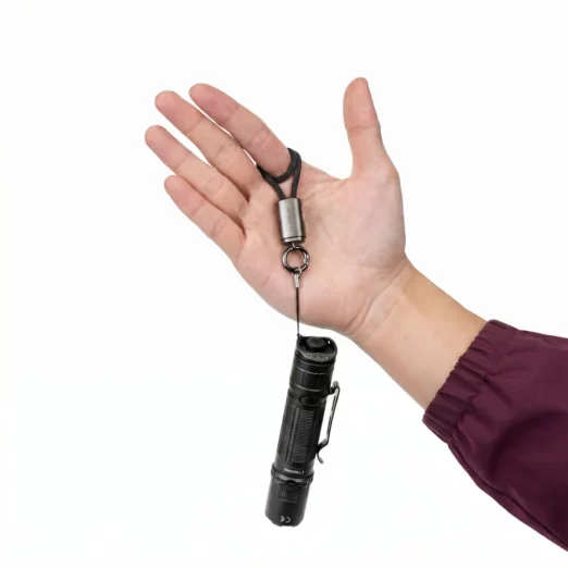 Small black compact flashlight on a cord and metal ring, held in an open palm with a maroon sleeve visible on the wrist.