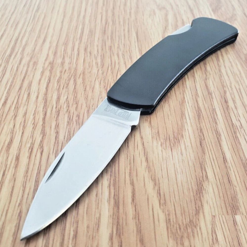 Folding pocket knife with a black handle and a silver blade partially open on a wooden surface