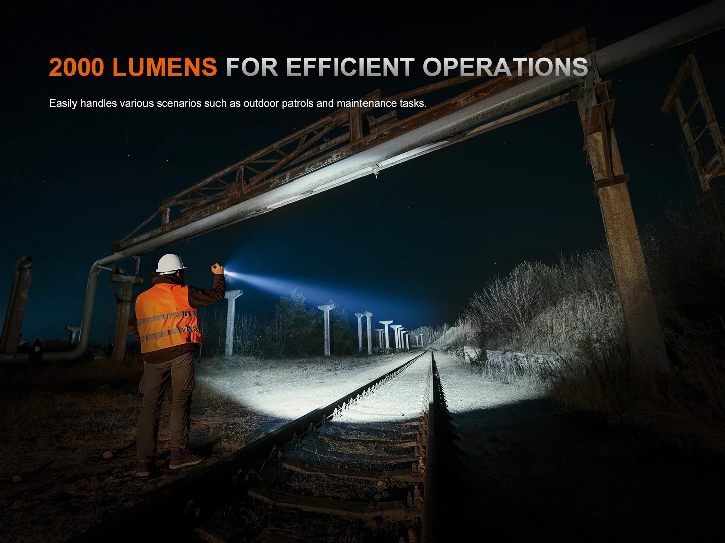 Night scene of a worker in an orange safety vest and white helmet shining a flashlight along rusted railroad tracks at night, with a large overhead structure and dark sky. The image includes the overlaid headline '2000 LUMENS FOR EFFICIENT OPERATIONS.'