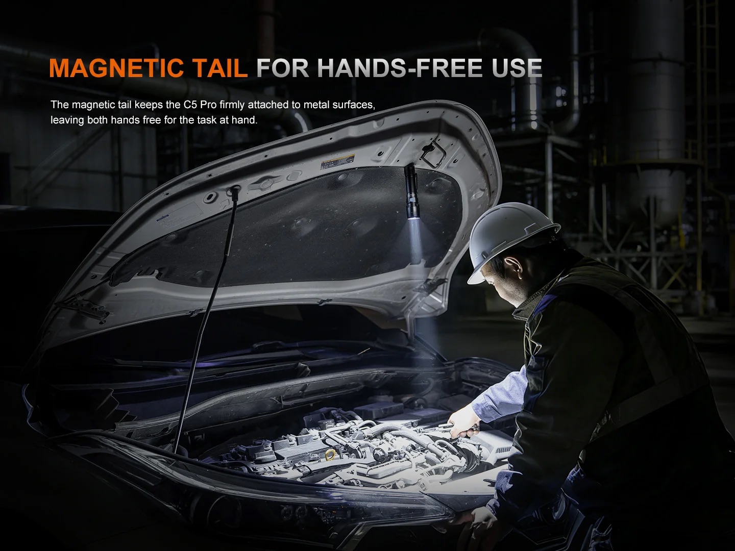 Mechanic in a dark workshop uses a magnetic tail light to illuminate the engine bay hands-free under the hood of a car.