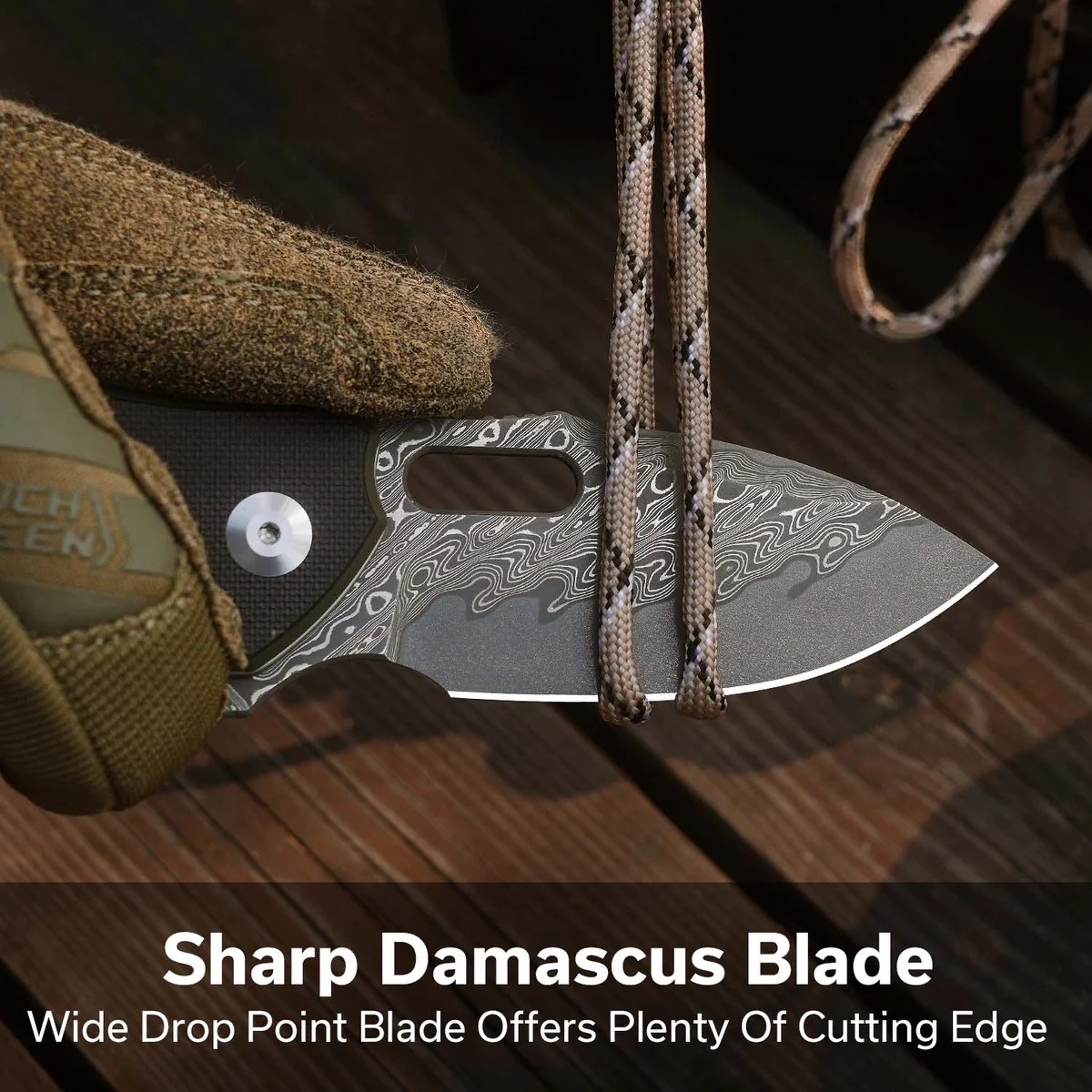 Close-up of a Damascus blade knife with a patterned edge and paracord draped over it on a wooden surface.