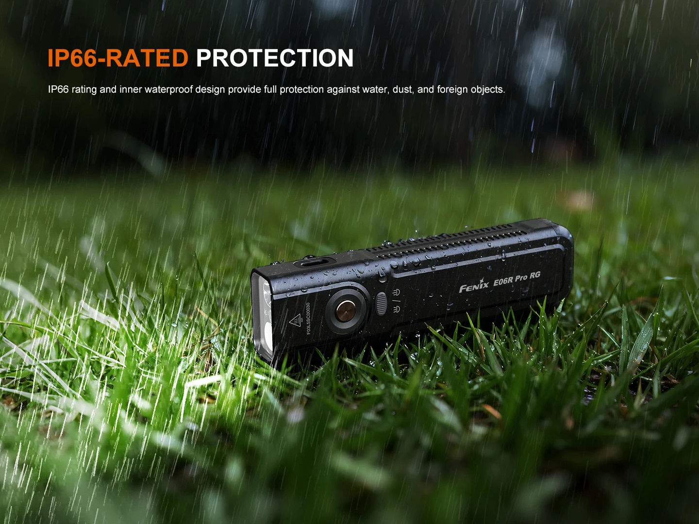 Black Fenix E06R Pro RG flashlight lying on wet grass in heavy rain, highlighting IP66-rated protection.