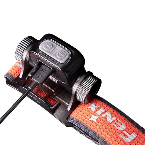 USB-powered battery charger with a cable attached, resting on an orange strap.