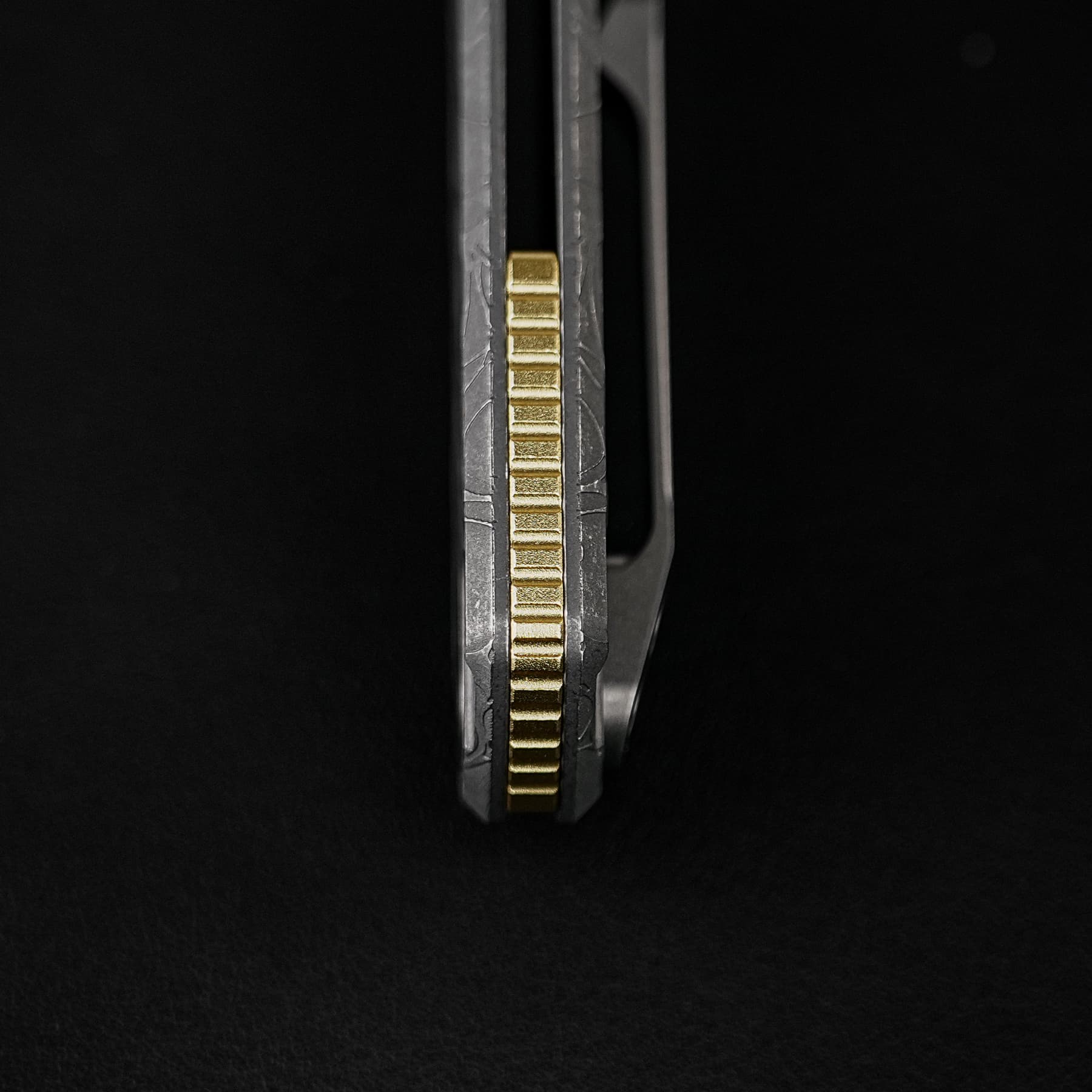 Close-up of a gold serrated gear centered between gray metal rails on a black background, vertical orientation.
