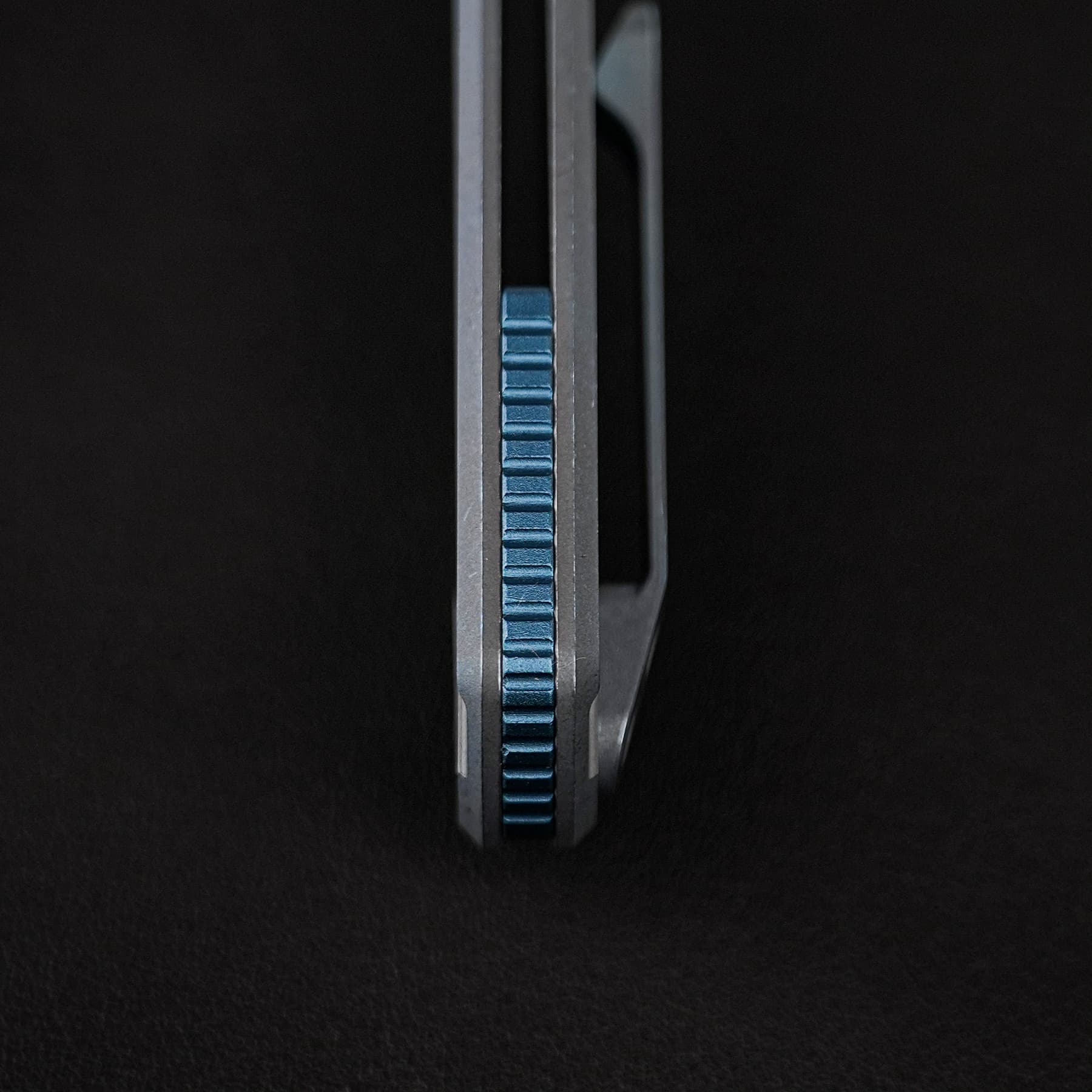Close-up of a metal tool with a vertical blue knurled adjustment wheel between two silver jaws, set against a black background.