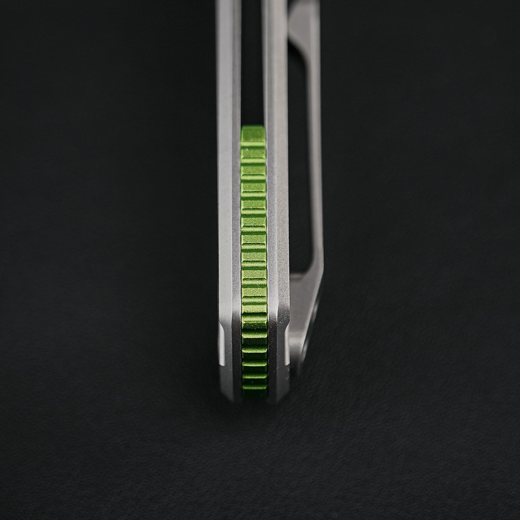 Macro close-up of a green grooved slider between two silver metal frames against a dark background, highlighting the mechanism's edge.