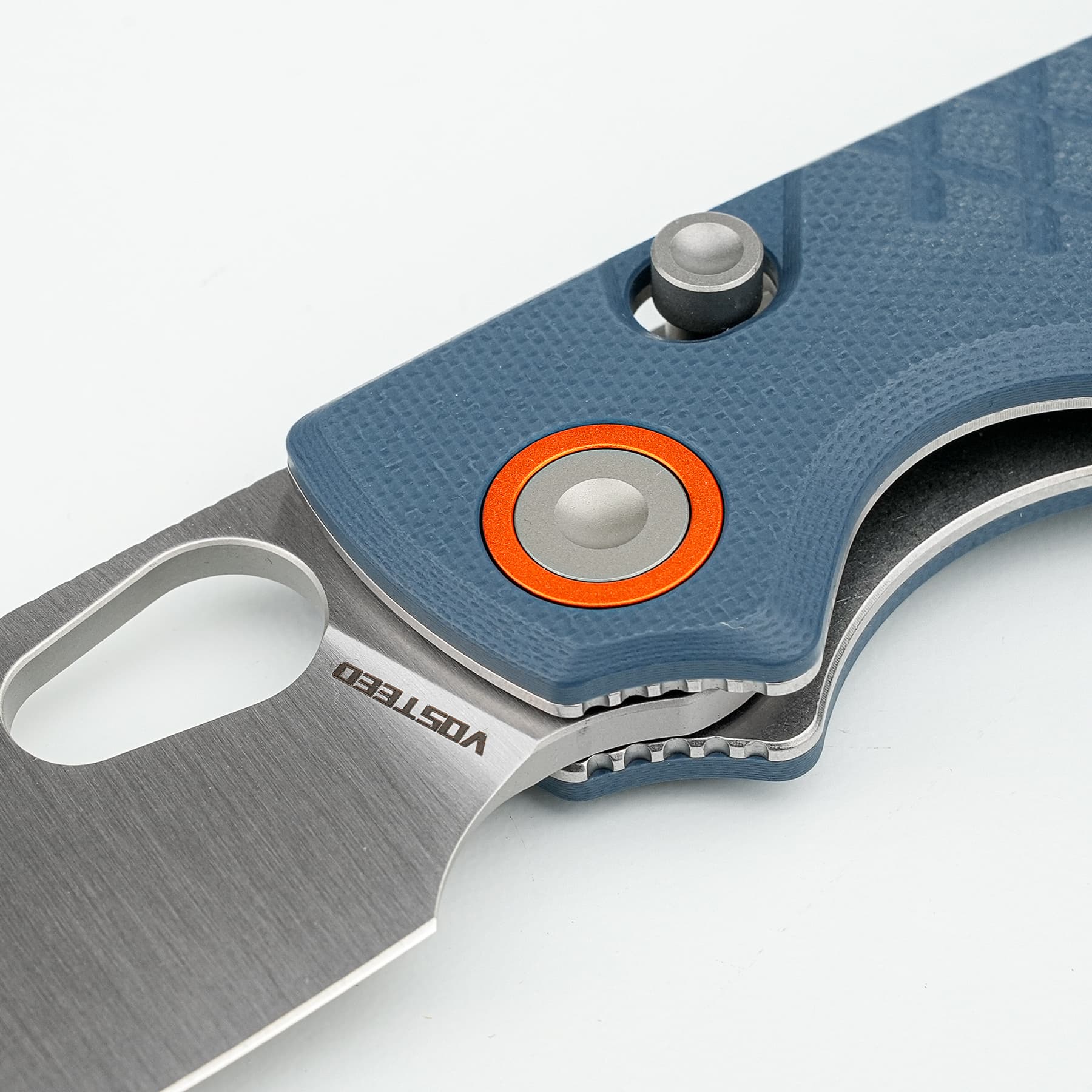 Close-up of a blue textured utility knife with a sharp metal blade and an orange-ringed circular button for adjustment/emergency lock.
