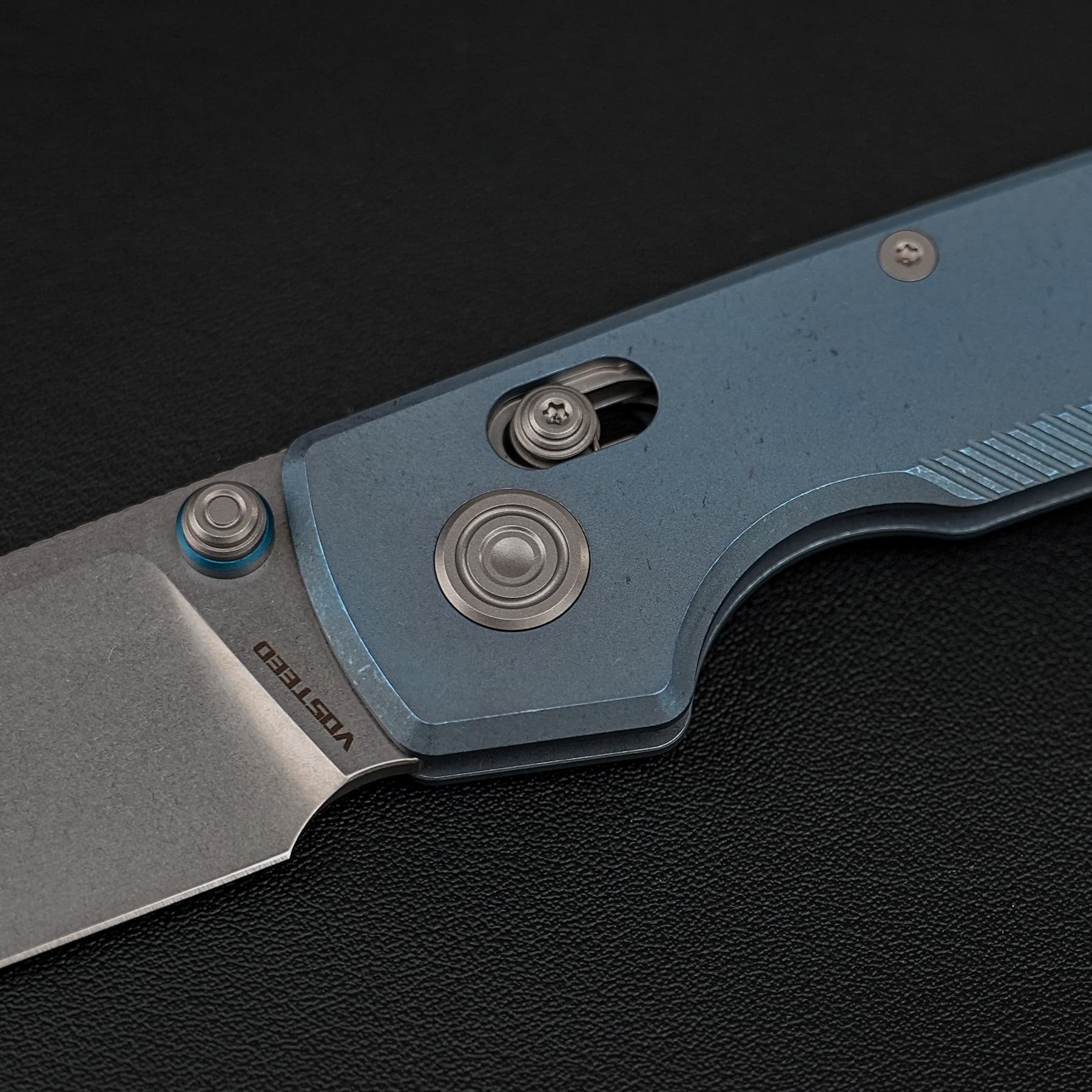 Close-up of a blue metal tool lever with round screws and circular metal caps on a dark textured surface.