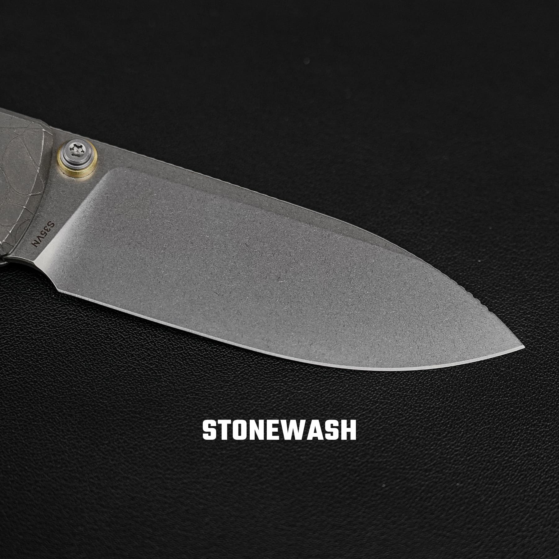 Close-up of a knife blade with a stonewashed finish on a dark textured background, with the word STONEWASH visible at the bottom.