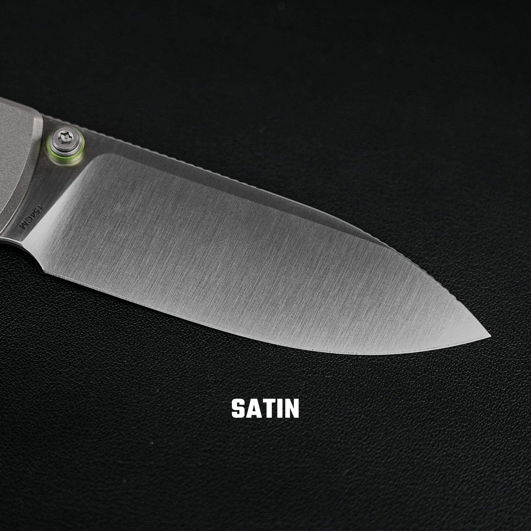Close-up of a satin-finished knife blade with a green pivot and textured metal surface on a black background; the word SATIN appears at the bottom.