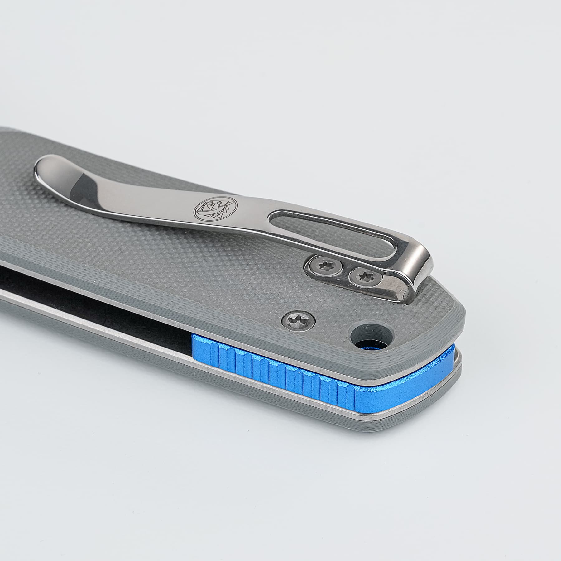 Close-up of a silver folding knife mechanism with a blue knurled grip on a textured gray base surface.