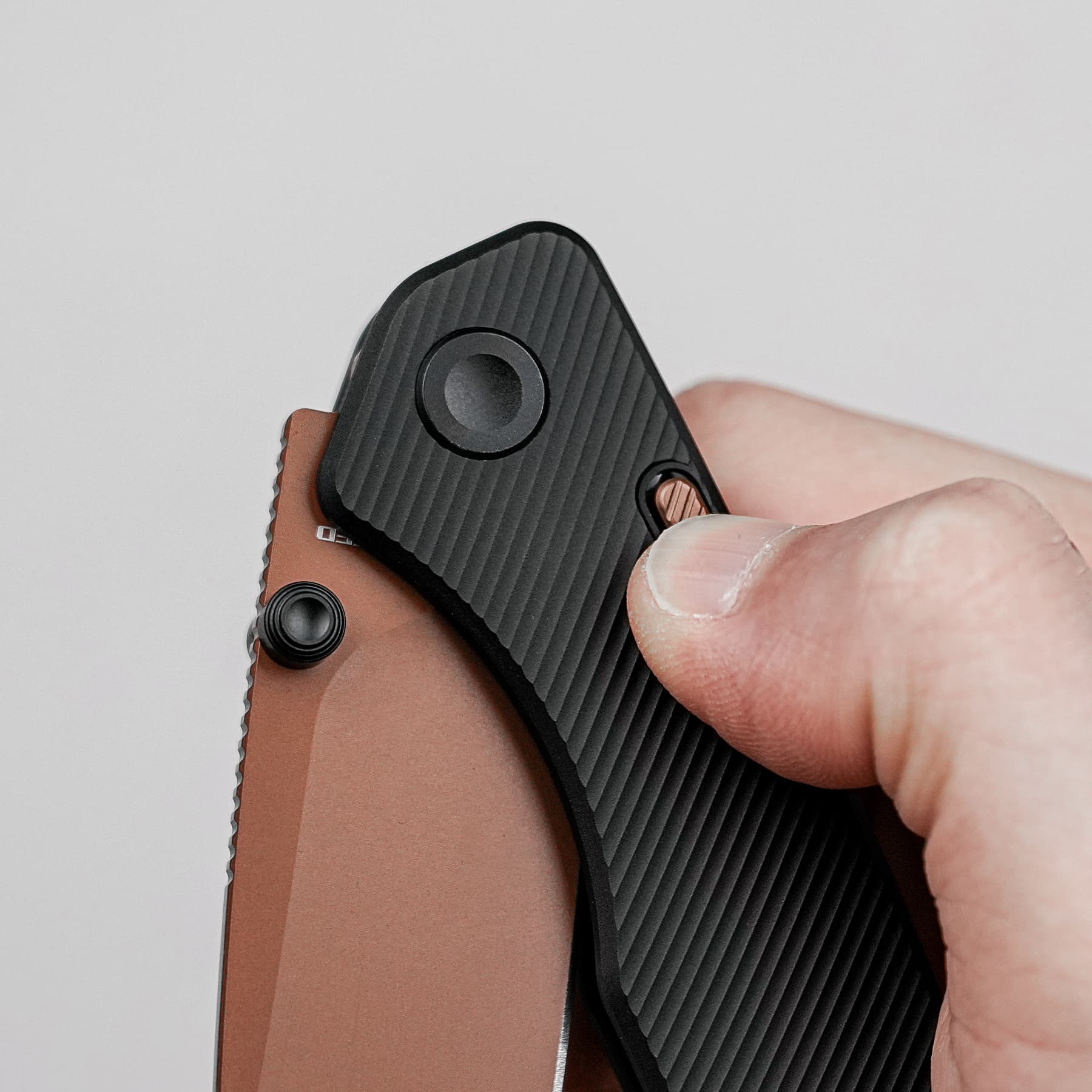 Close-up of a hand gripping a small folding knife with a textured black handle and brown/satin scale, showing the pivot and thumb area.