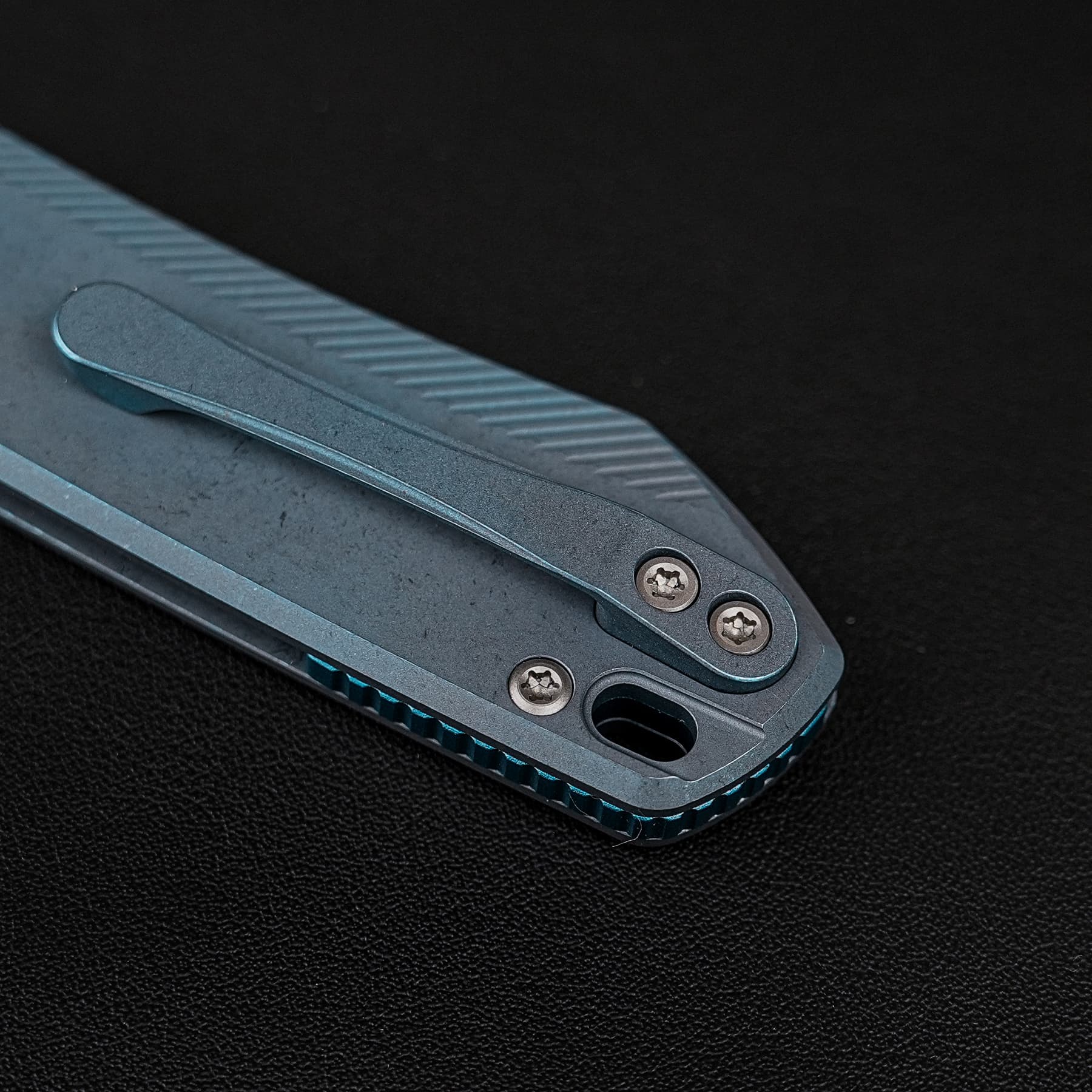 Close-up of a blue folding multitool with exposed screws on a dark textured surface, partially opened edge visible.
