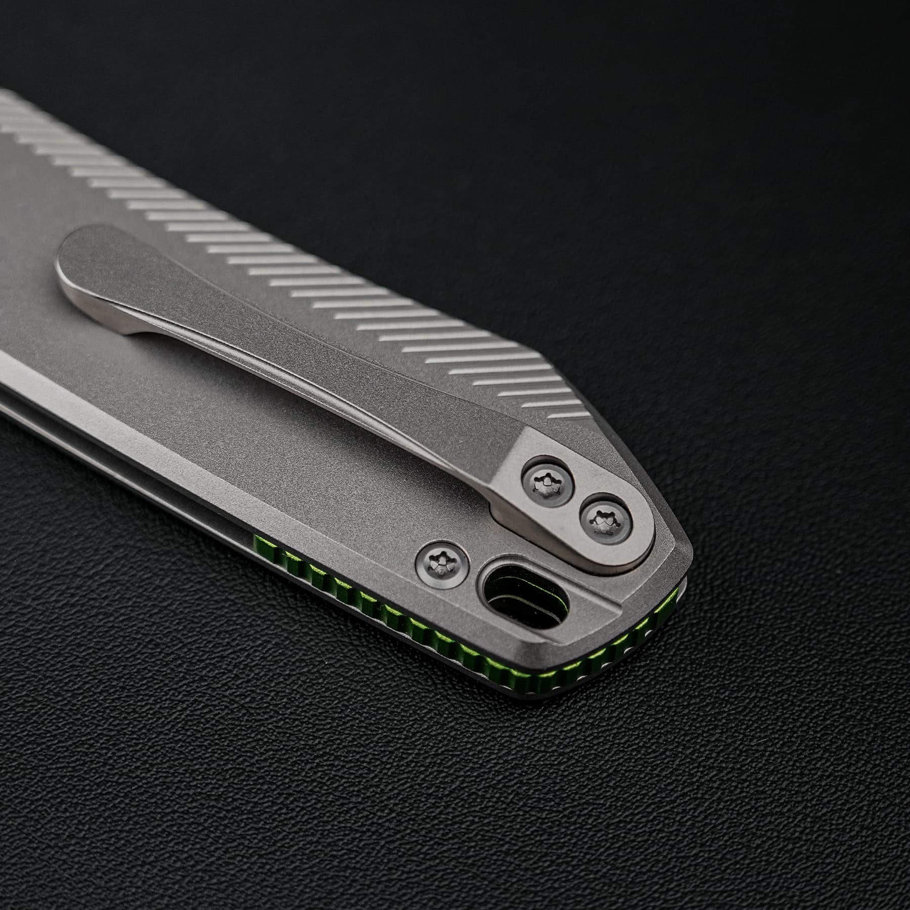 Close-up of a silver folding knife handle with a ribbed grip and visible screws on a dark surface.