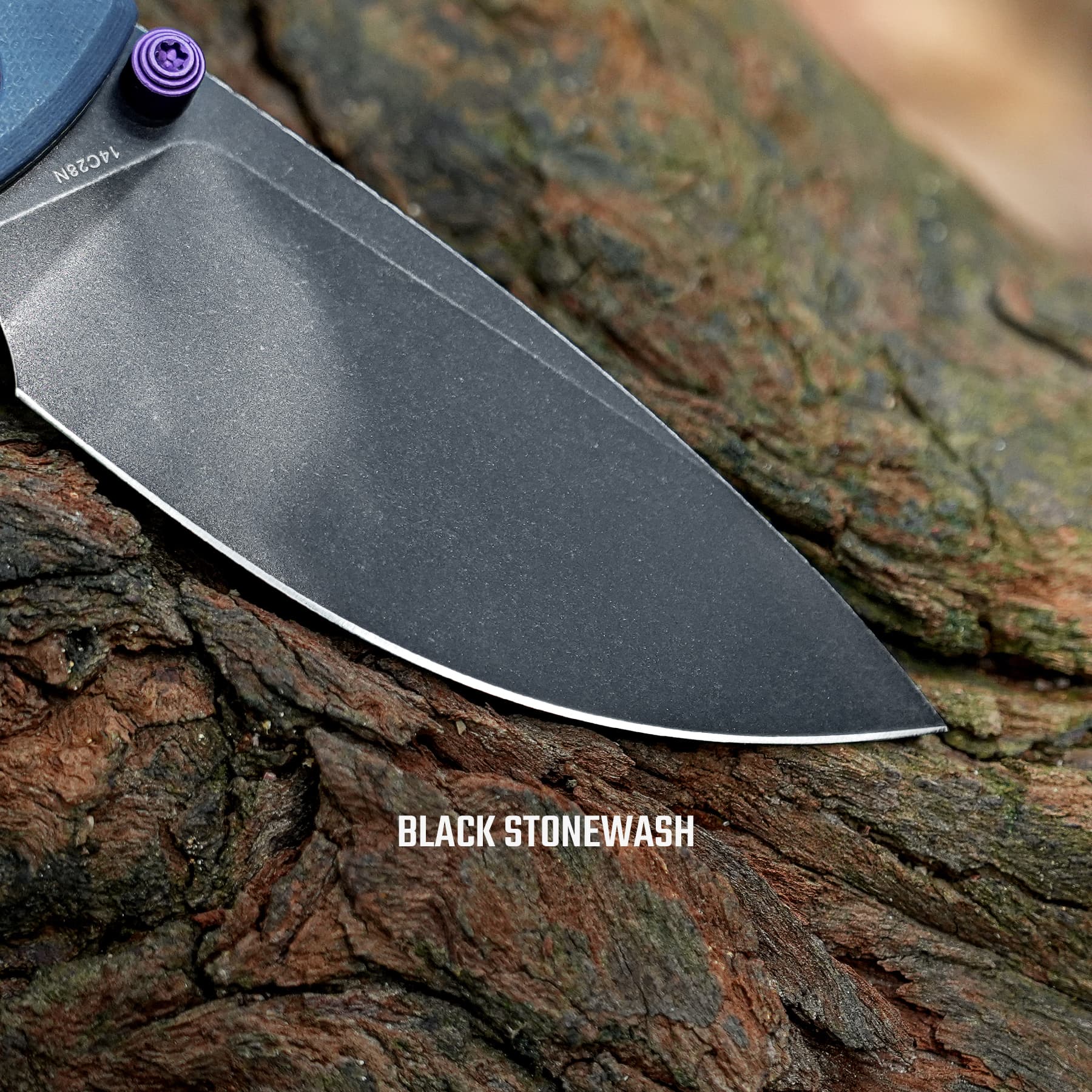 Close-up of a knife blade with a black stonewash finish resting on rough tree bark; the caption 'BLACK STONEWASH' is visible.