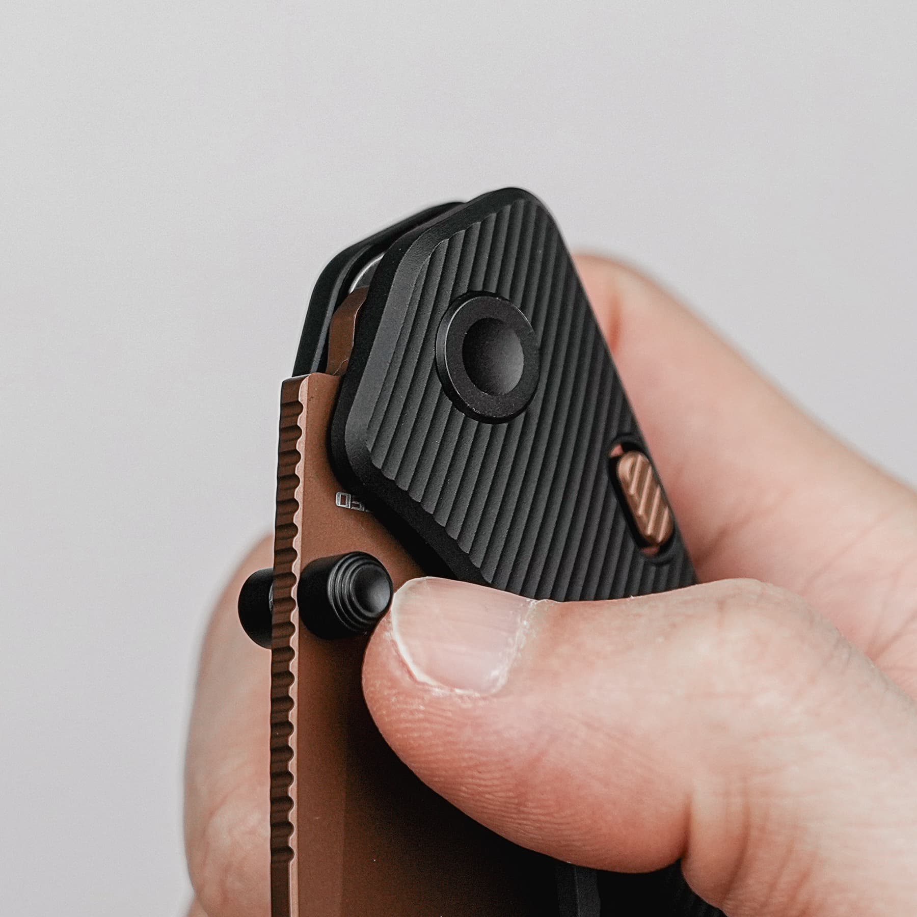 Close-up of a black, ribbed pocketknife with copper-colored hardware being held between fingers