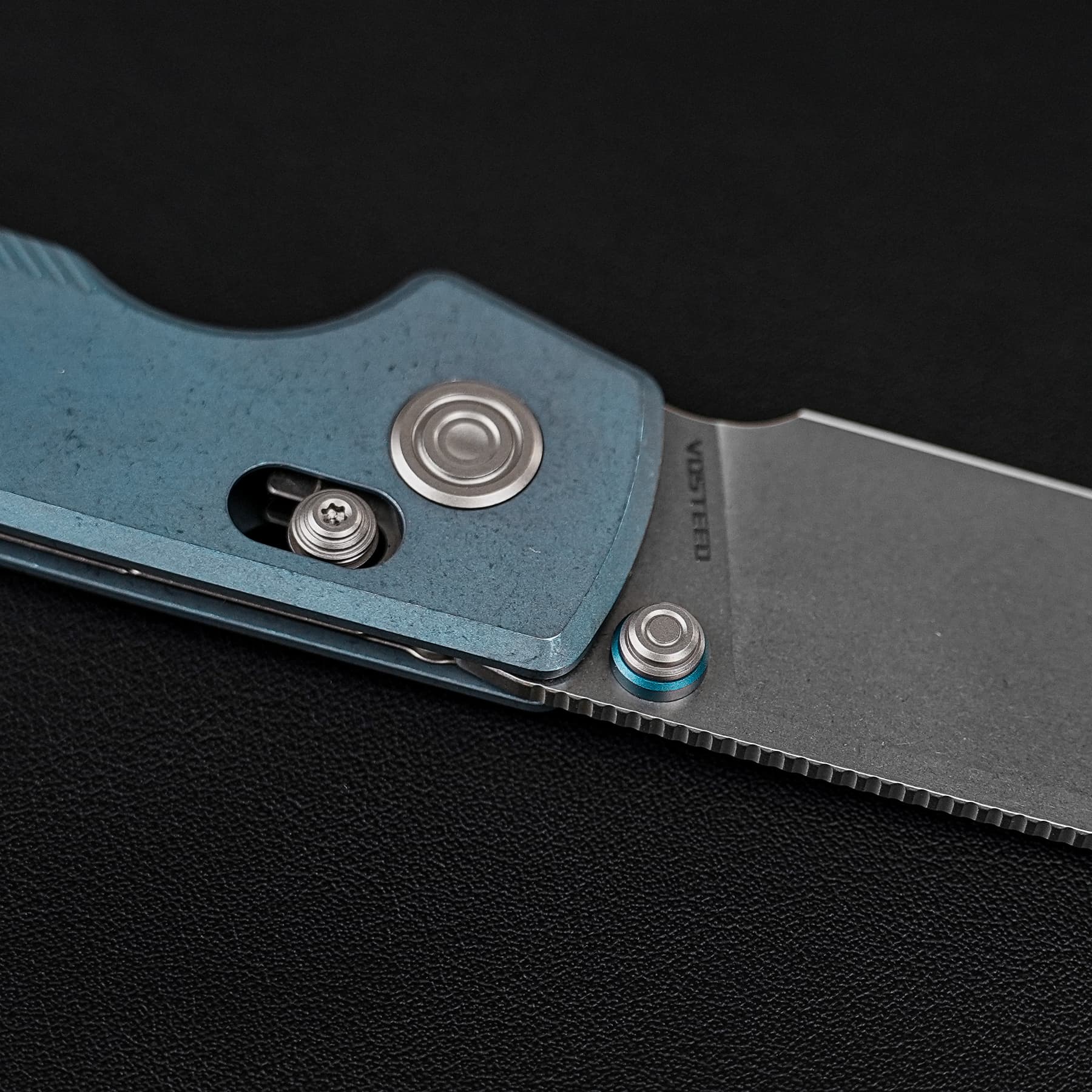 Close-up of a blue folding knife blade with exposed serrated edge and screws against a black background