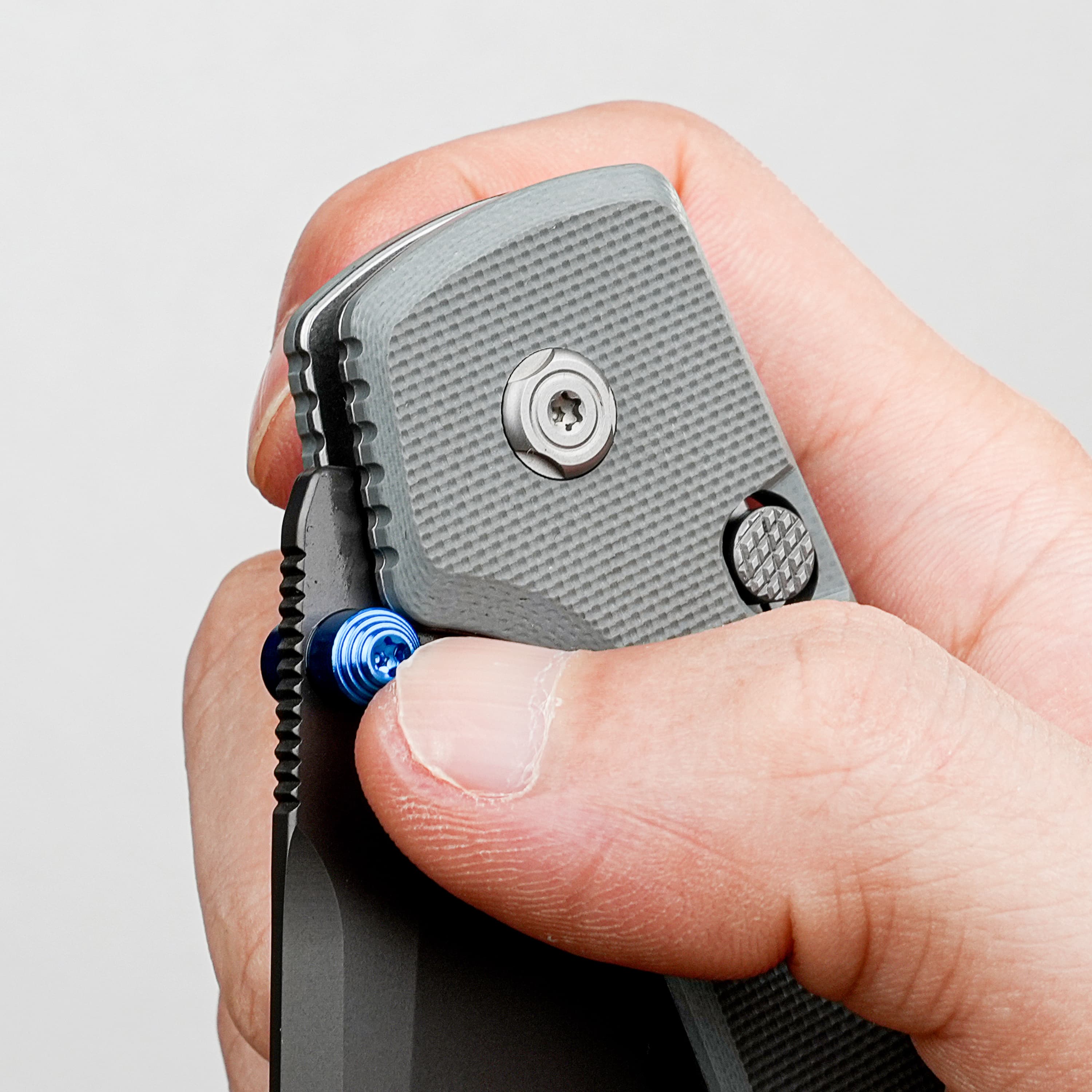 Close-up of a hand gripping a gray, textured multitool with blue knobs.