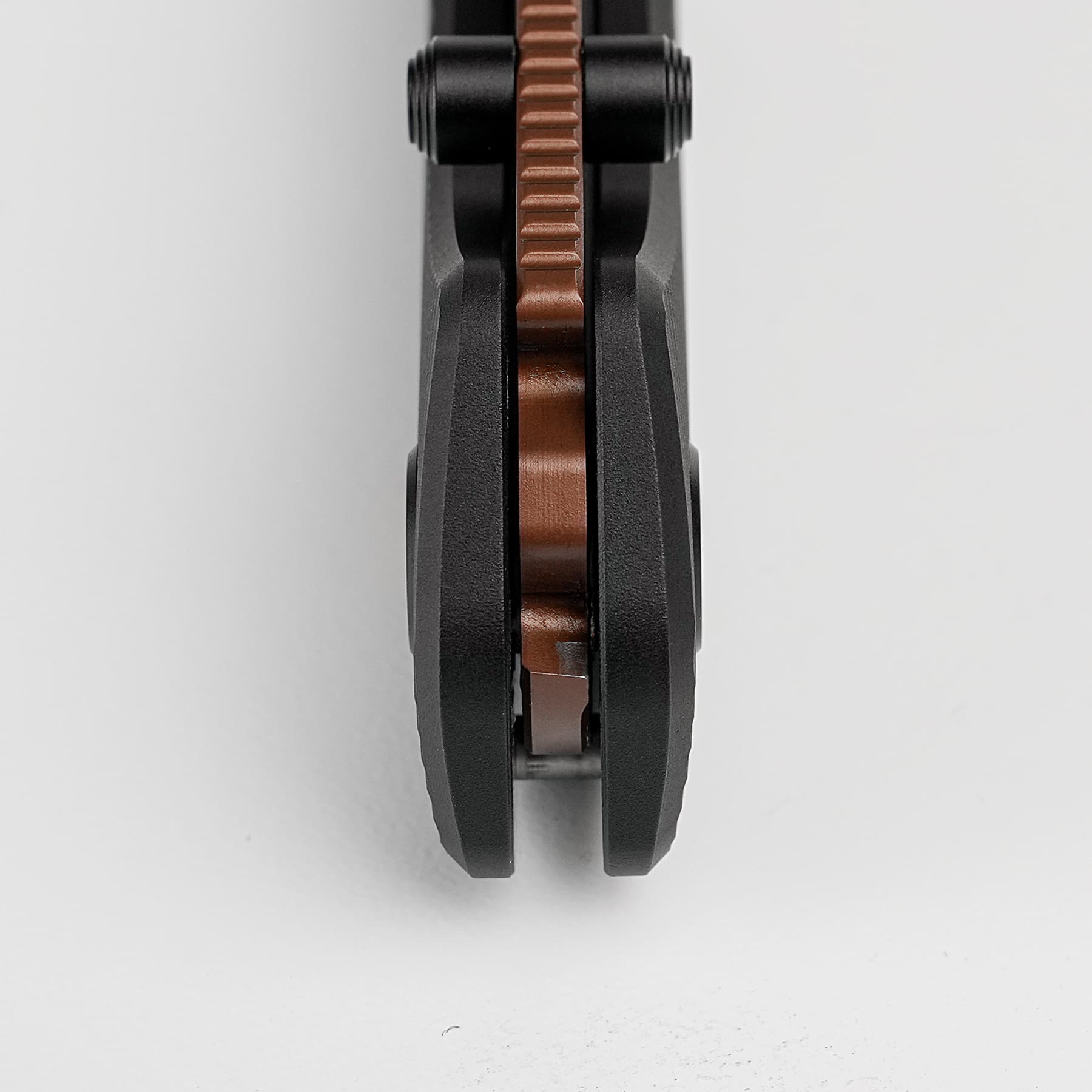 Close-up of a brown serrated gear between two black metal components, viewed head-on from between the parts.