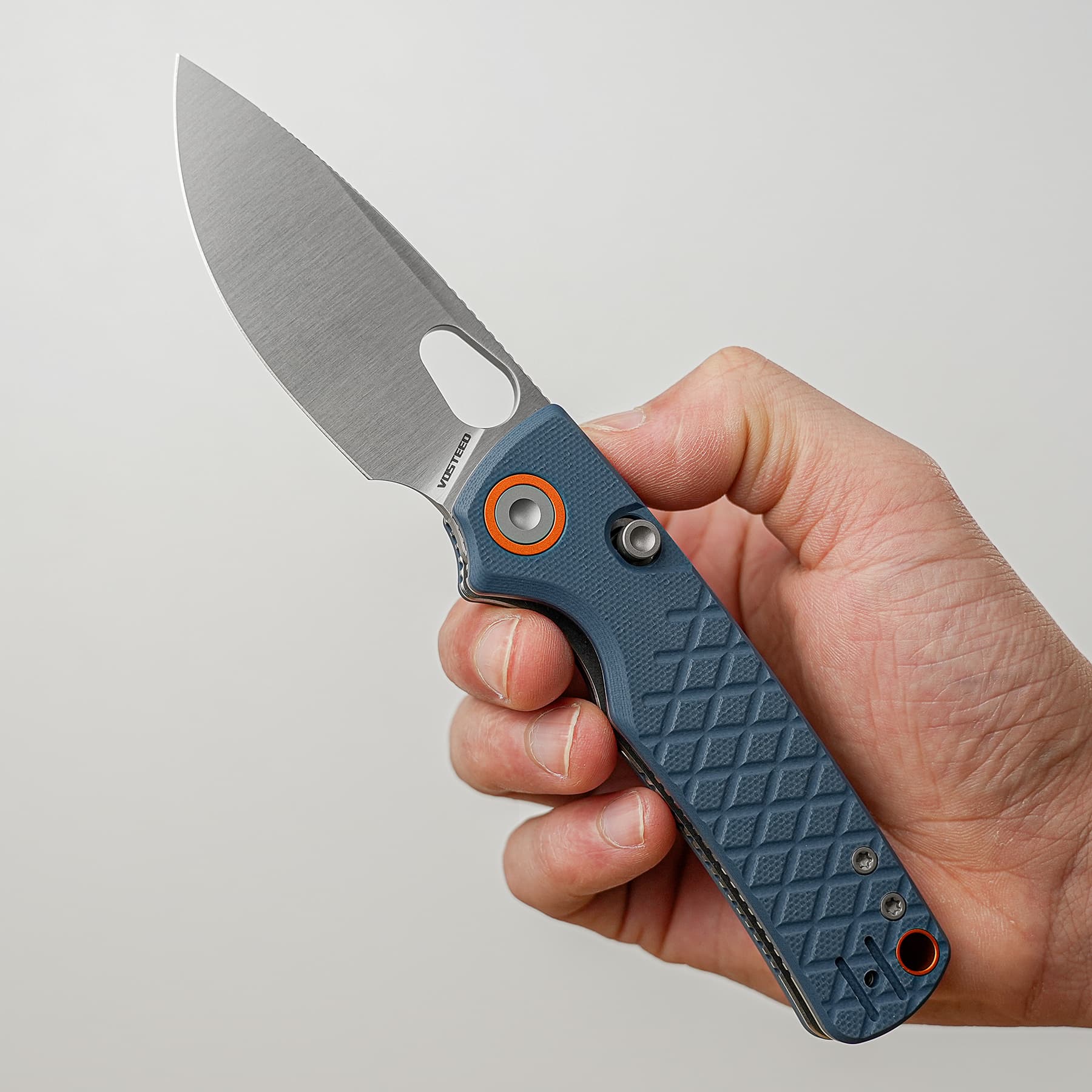 Close-up of a folding knife with a blue textured handle being held between the thumb and forefinger, blade partially open and pointed left.