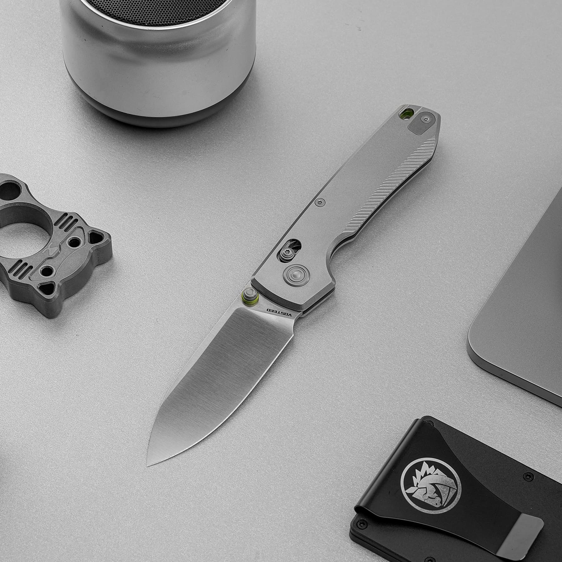 Close-up of a metallic folding knife on a gray workspace with small tool components nearby.