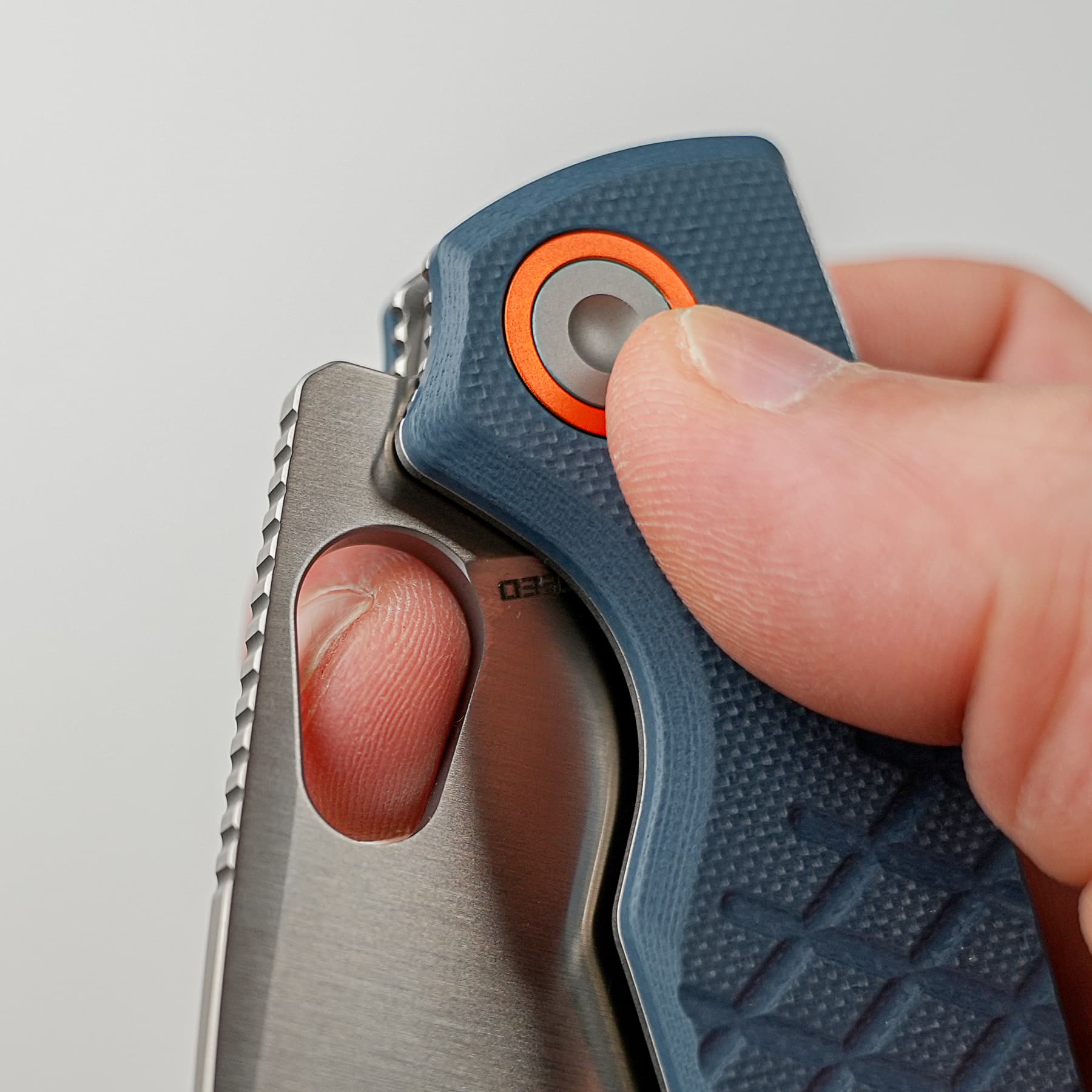 Close-up of a finger pressing an orange-ringed button on a blue textured device; a metal clip is visible nearby.
