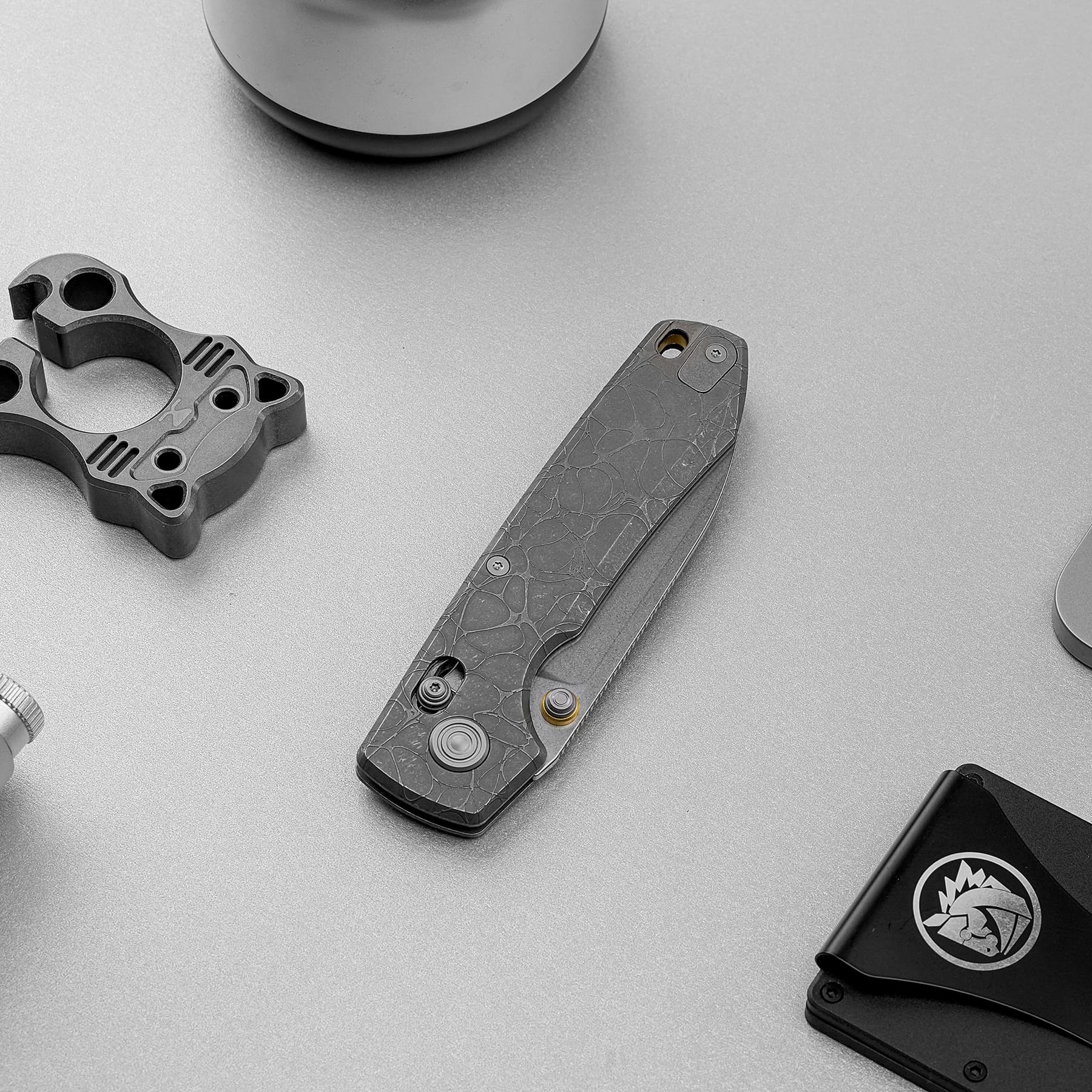 Close-up of a folding knife with a gray marbled handle on a light gray surface, with metal hardware nearby.