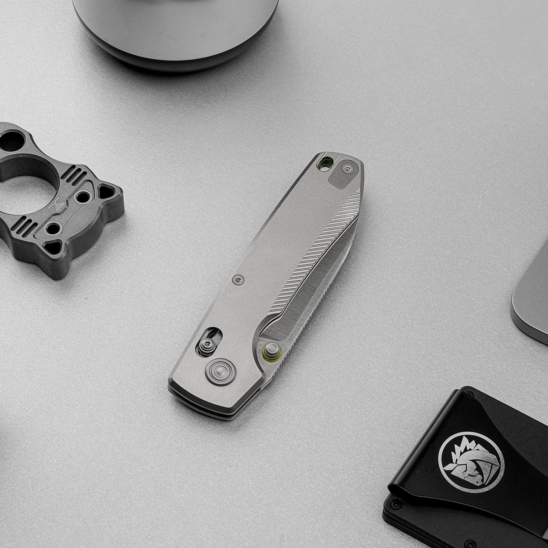 Top-down view of a metal folding knife sharpener and a separate gray tool part on a gray textured surface.