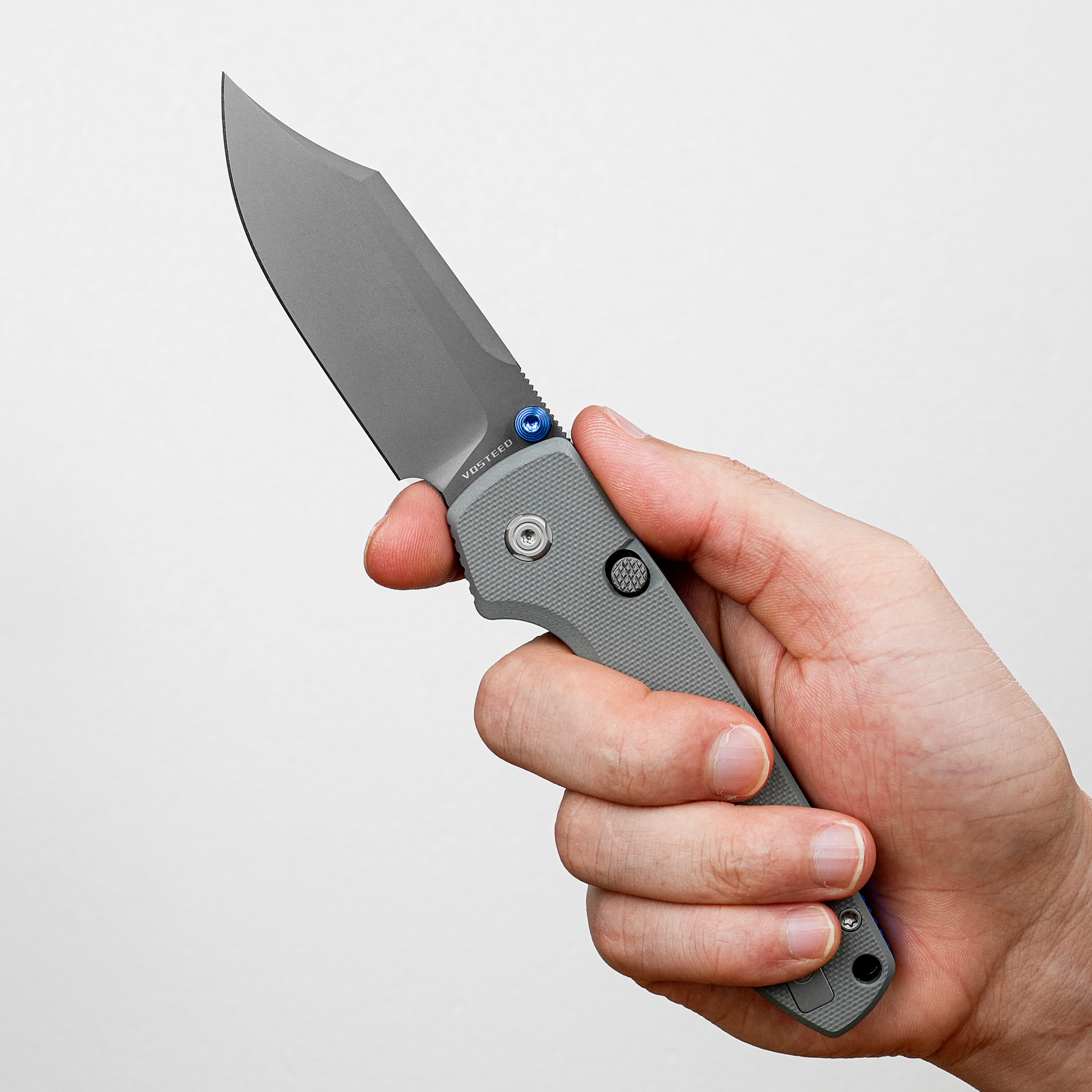 Close-up of a hand holding a grey folding knife with the blade partially extended against a light background.