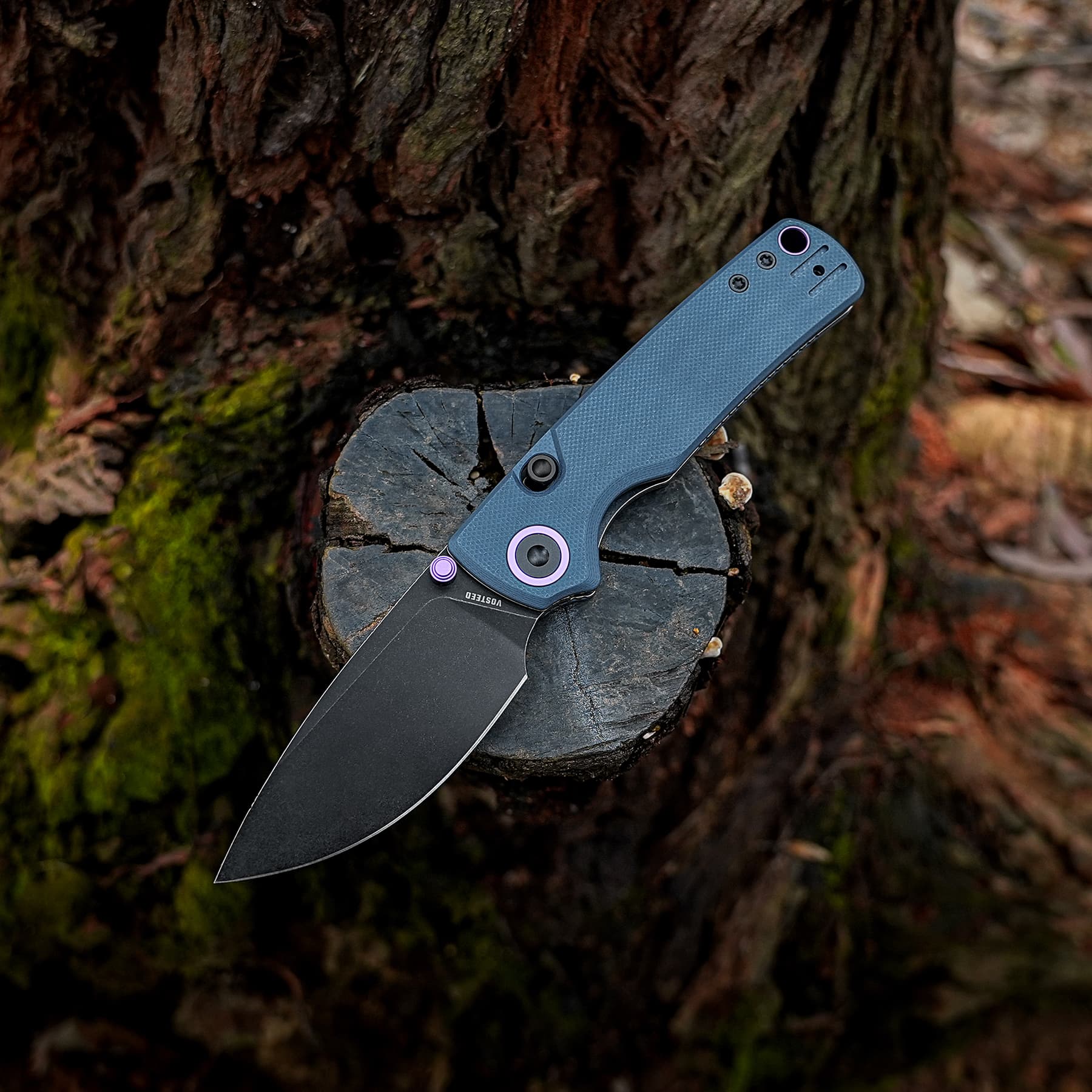 Blue textured folding knife resting on a tree stump outdoors in a forest setting.