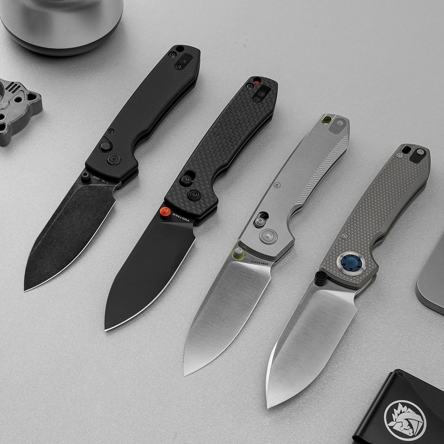 Line of four folding knives with different handle textures arranged diagonally on a gray surface, blades exposed.