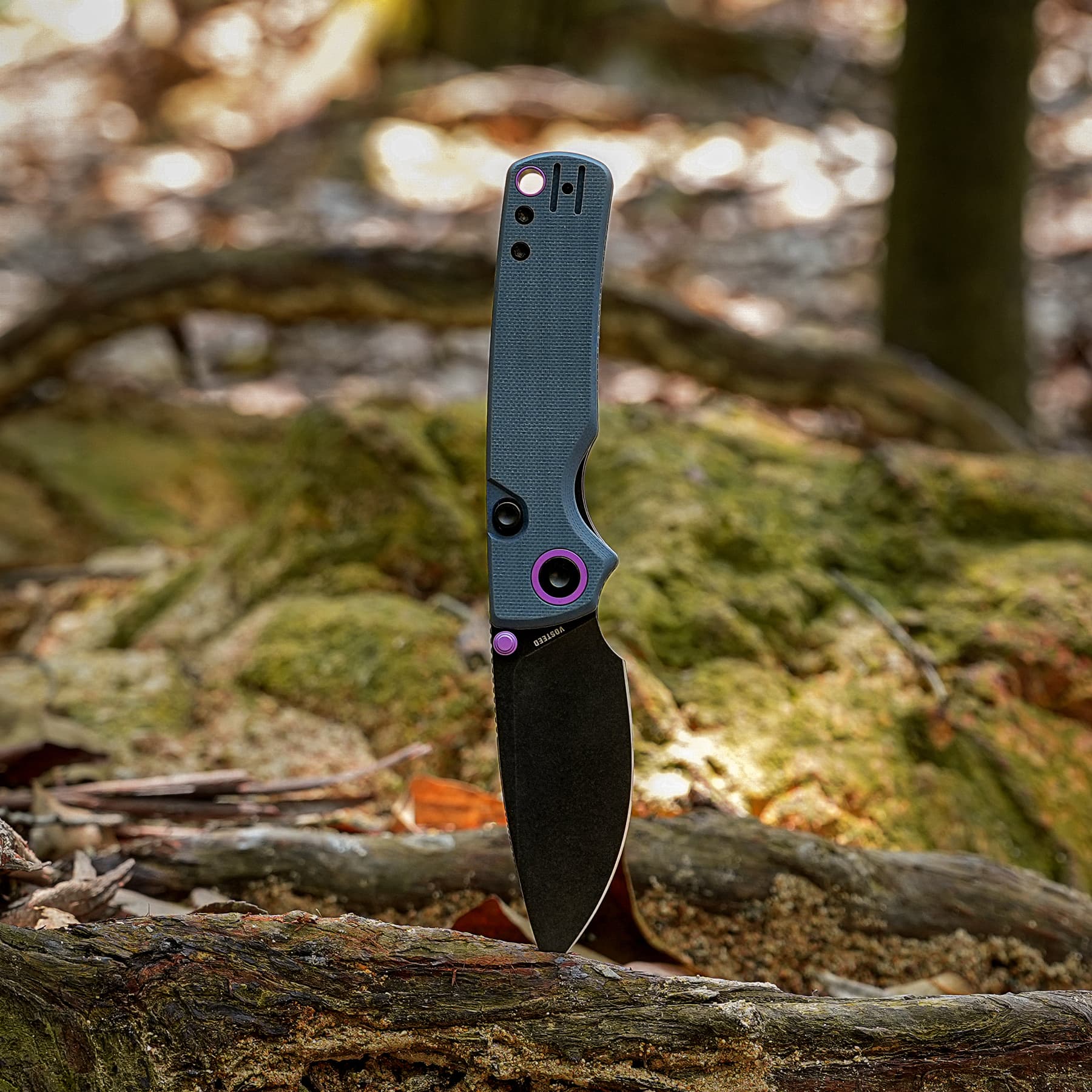 Folding knife standing upright in a mossy log with a blurred forest background.