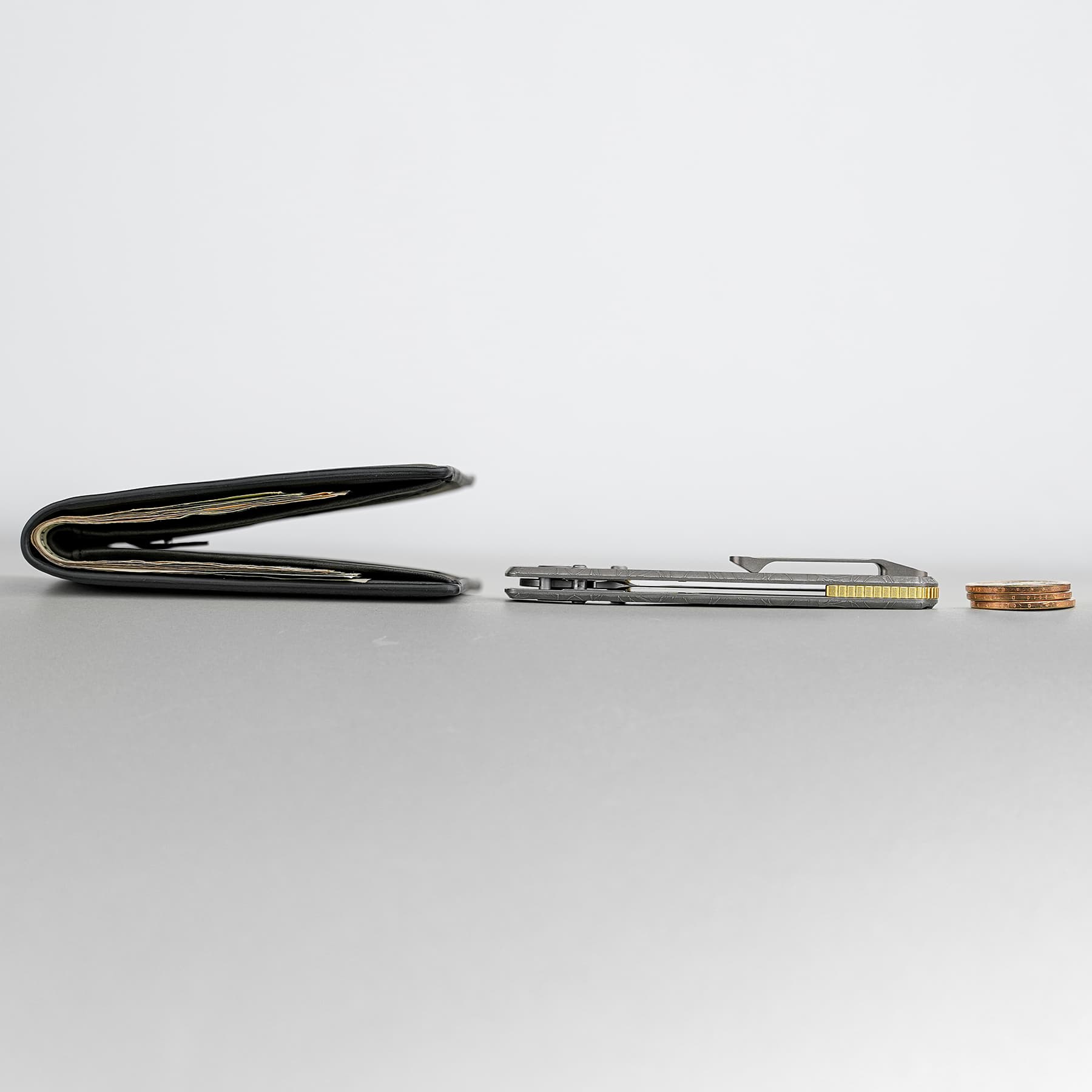 Open black wallet with cash and cards visible on a gray surface, coins and a metal cardholder/staple to the right.