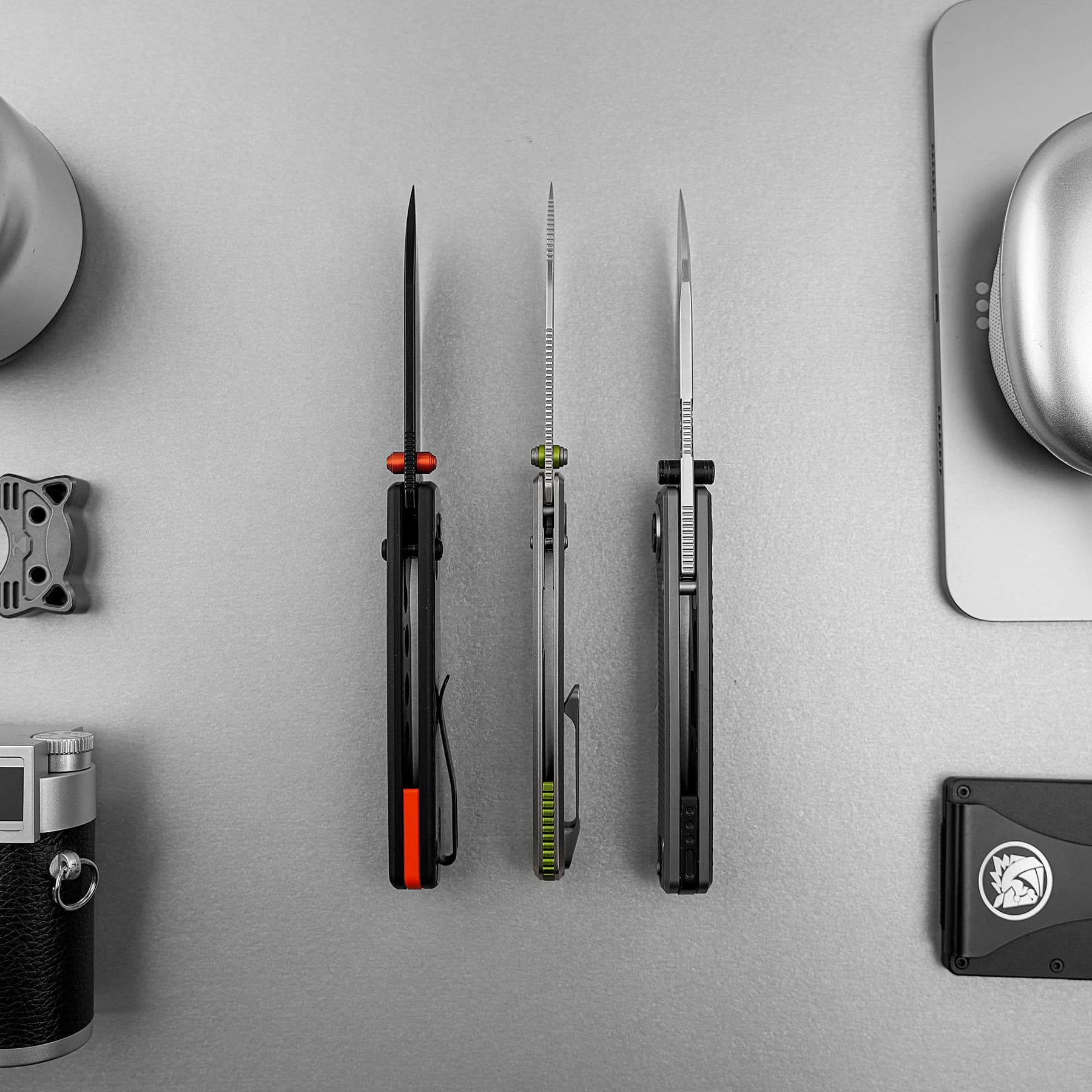 Three craft knives with colored grips standing upright on a gray work surface.