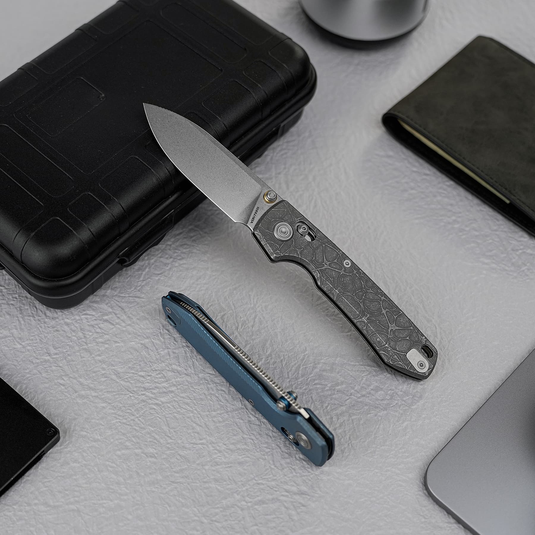 Partially opened folding knife with a textured handle resting on a black hard case.