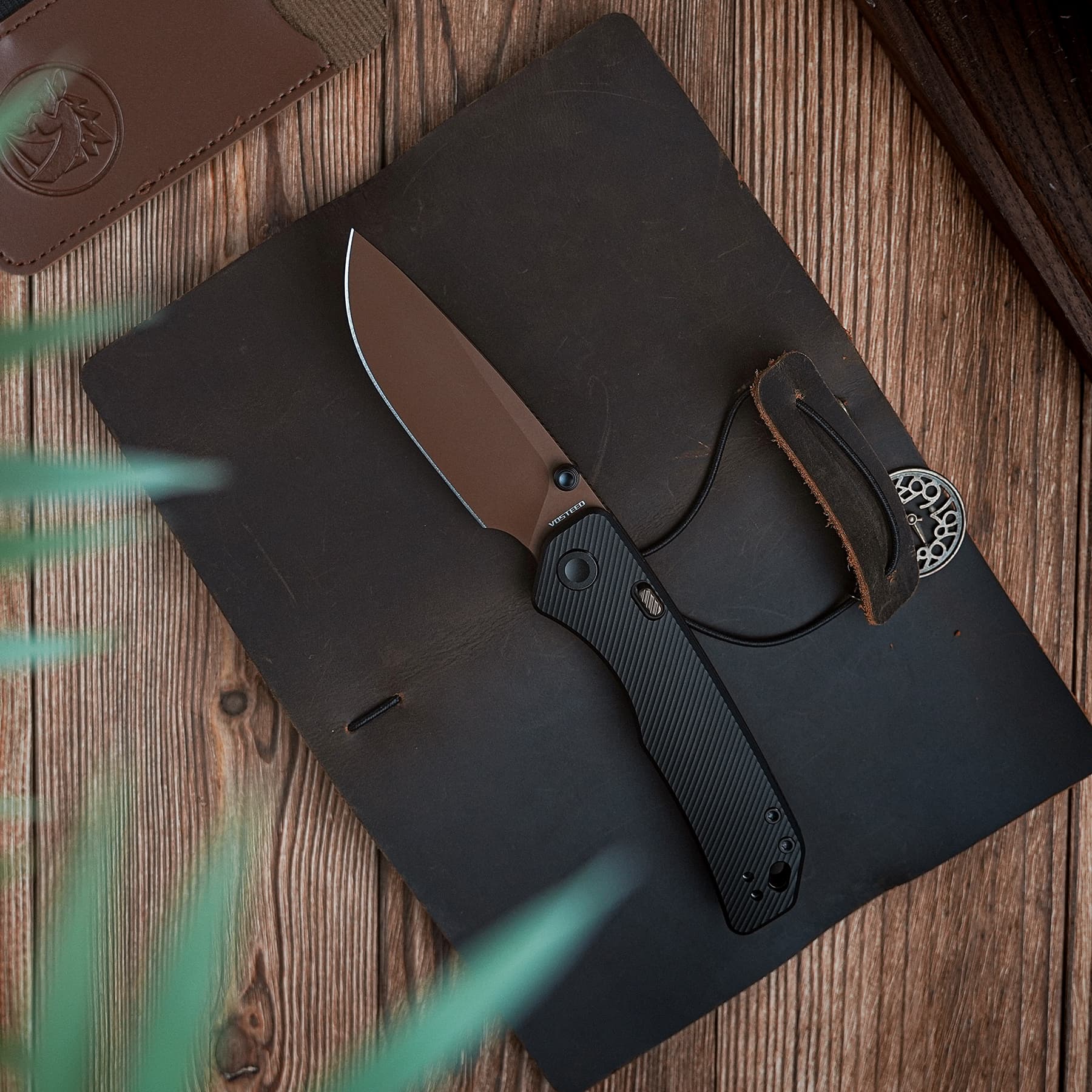 Folding knife with a brown blade and black handle resting on a black notebook on a wooden table.