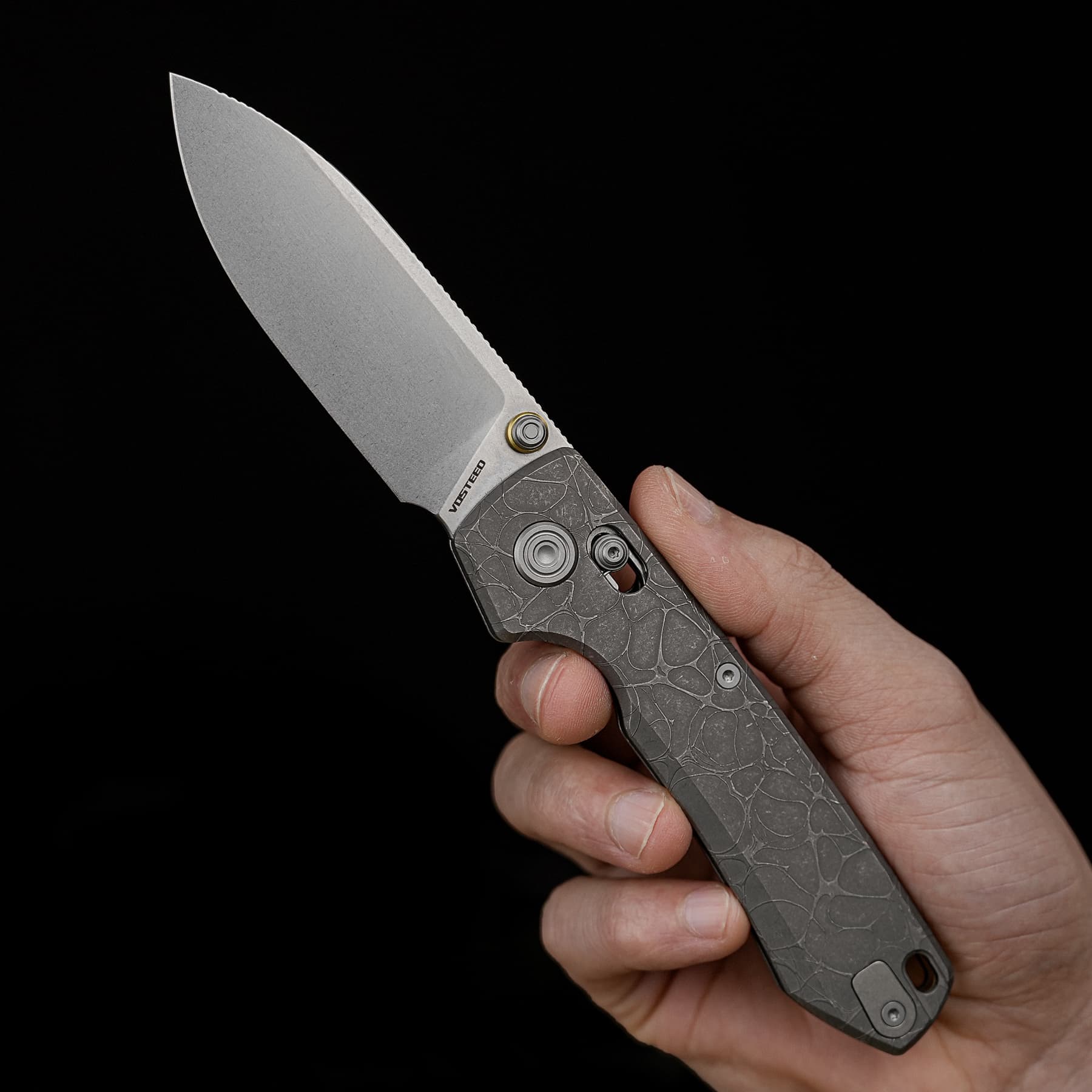 Close-up of a silver folding knife blade being held by a hand against a solid black background.