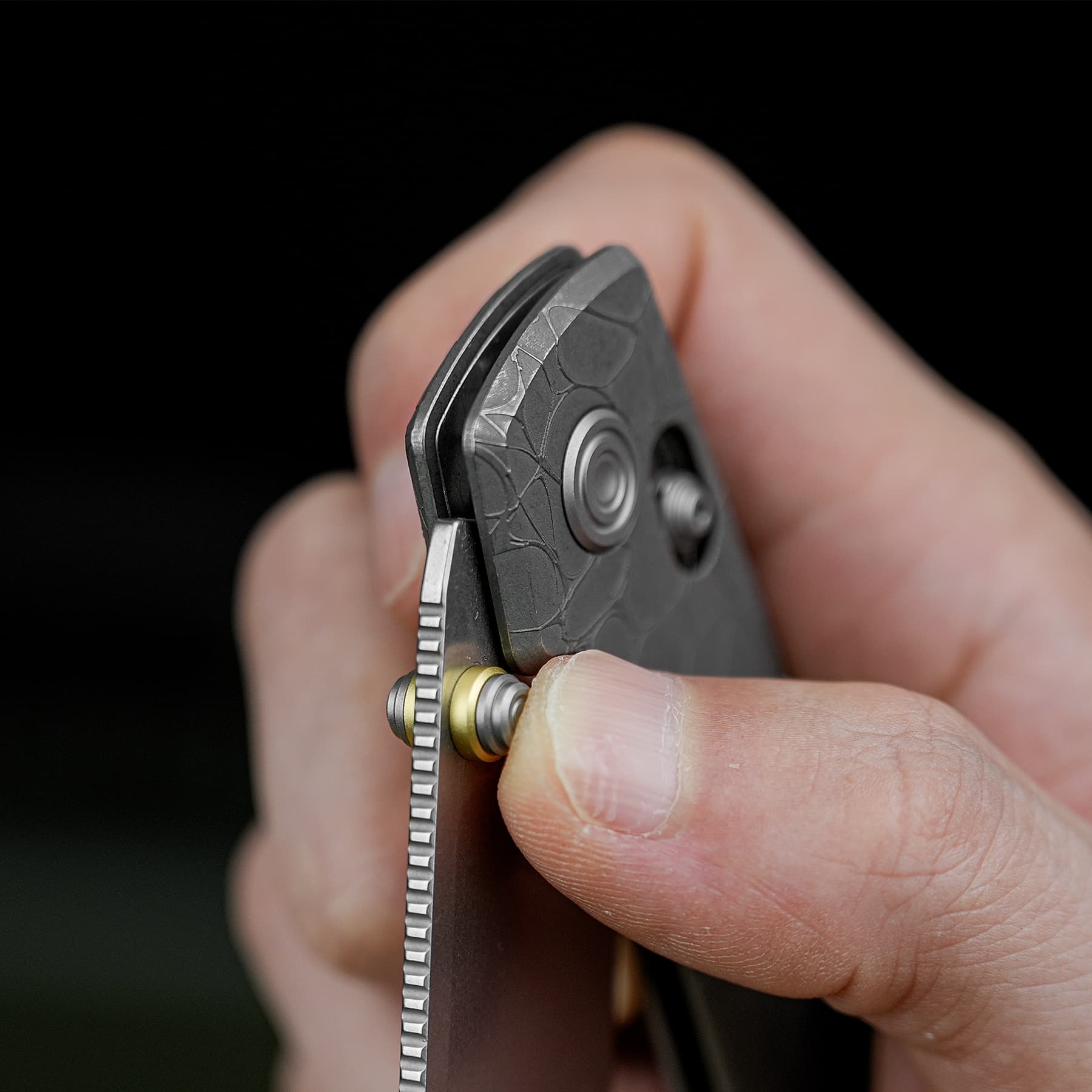 Close-up of a finger and thumb holding a compact folding knife; the blade is folded into the textured gray handle against a dark background.