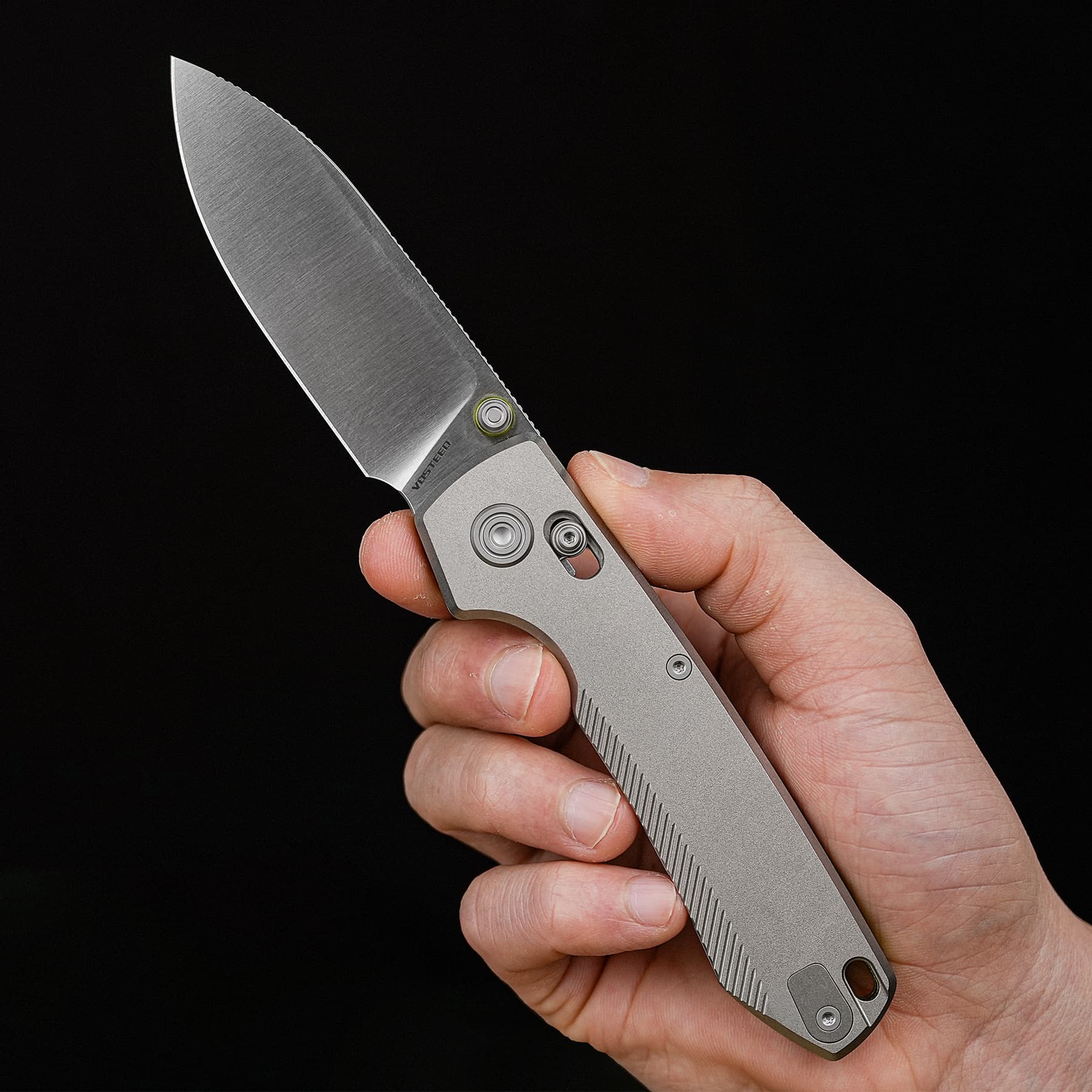 Close-up of a hand holding a folding knife with a silver blade against a black background.