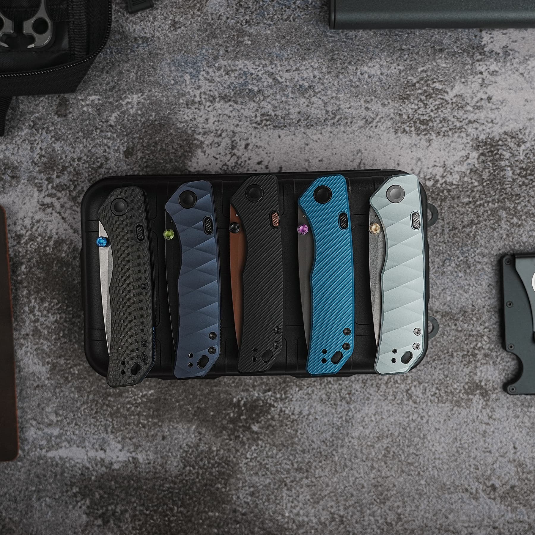 Top-down view of several textured smartphone cases in blue, gray, brown, and black arranged in a black tray on a gray surface