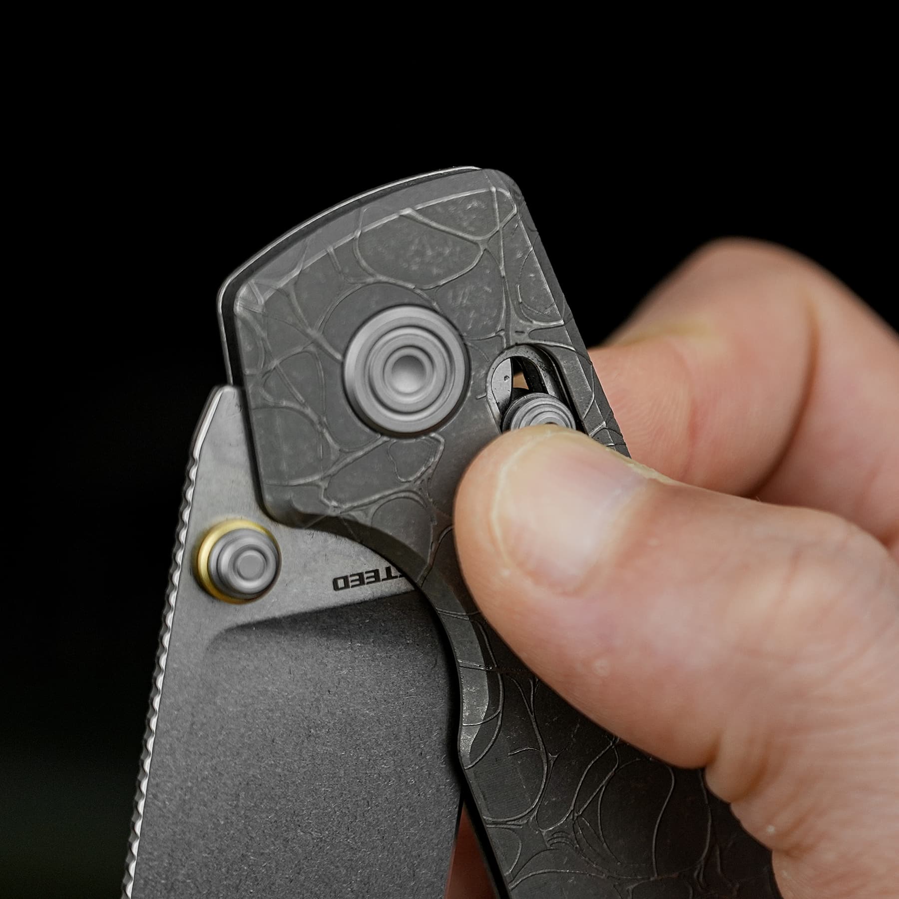 Close-up of a hand gripping a gray folding knife with a textured handle against a black background.