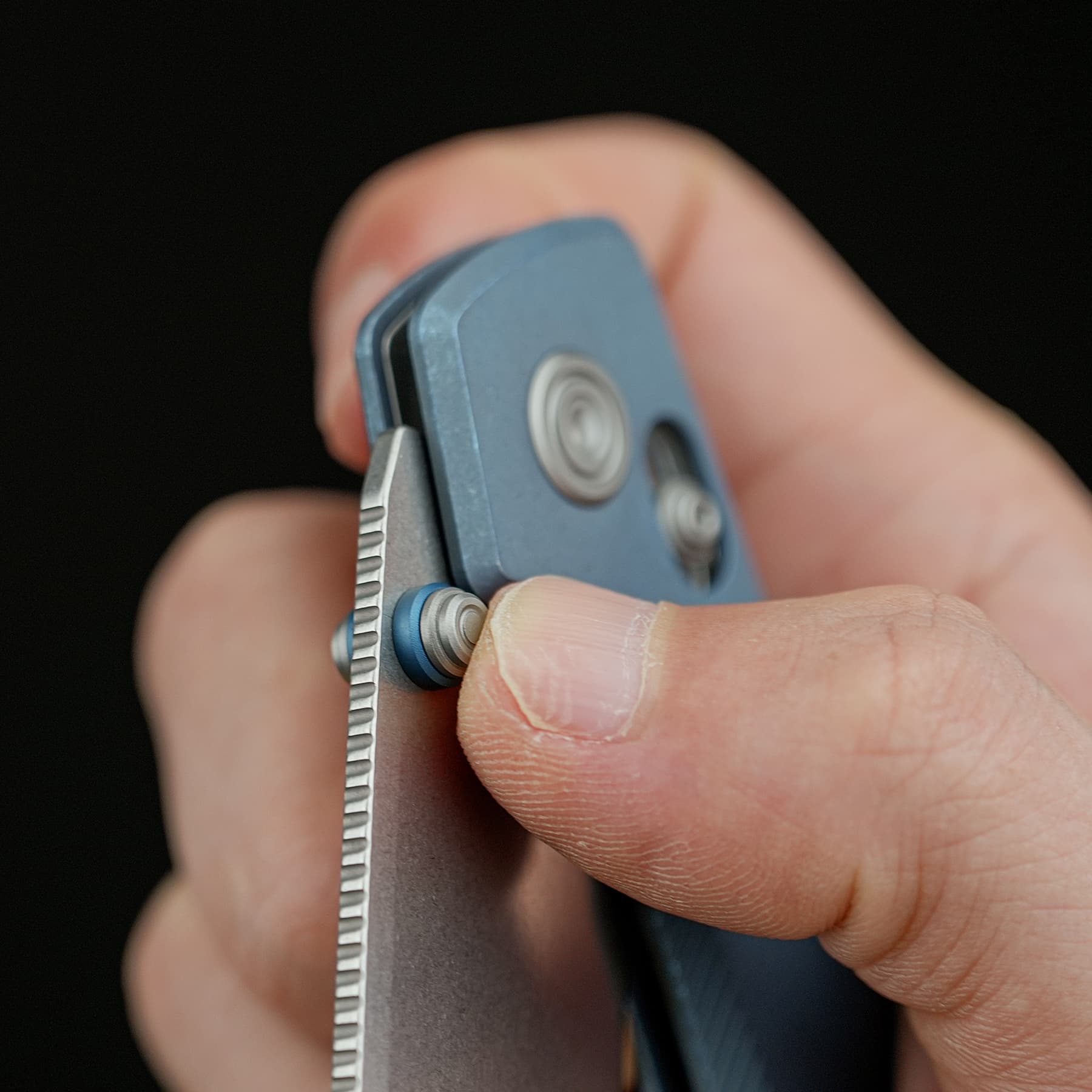 Close-up of fingers using a small blue metal tool to push a pin out of a steel watch band link for resizing.
