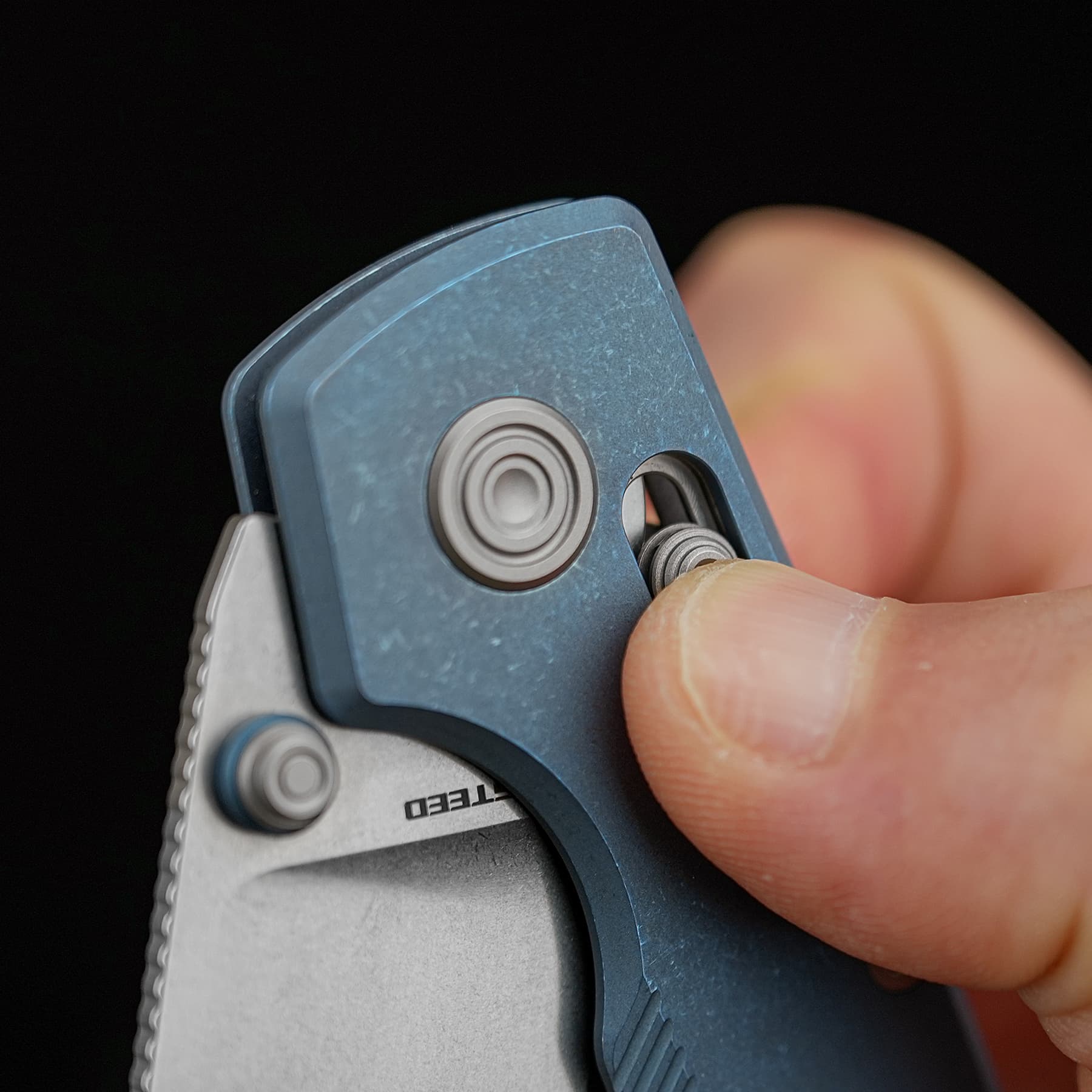 Close-up of a hand extending the blade on a blue retractable utility knife, focusing on the circular mechanism and blade edge.