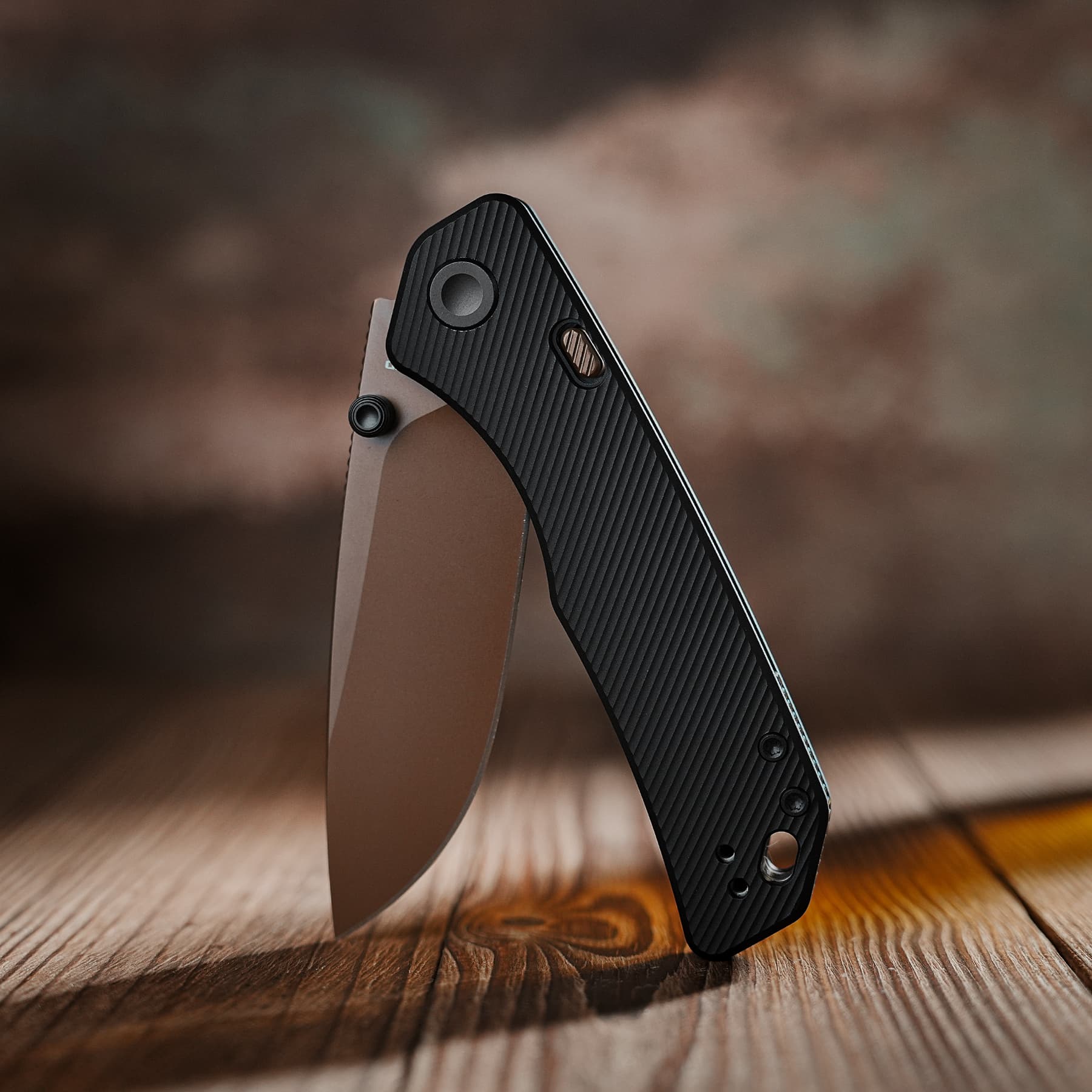 Close-up of a black textured folding knife held against a wood surface, showing the ribbed handle and visible pivot screw.