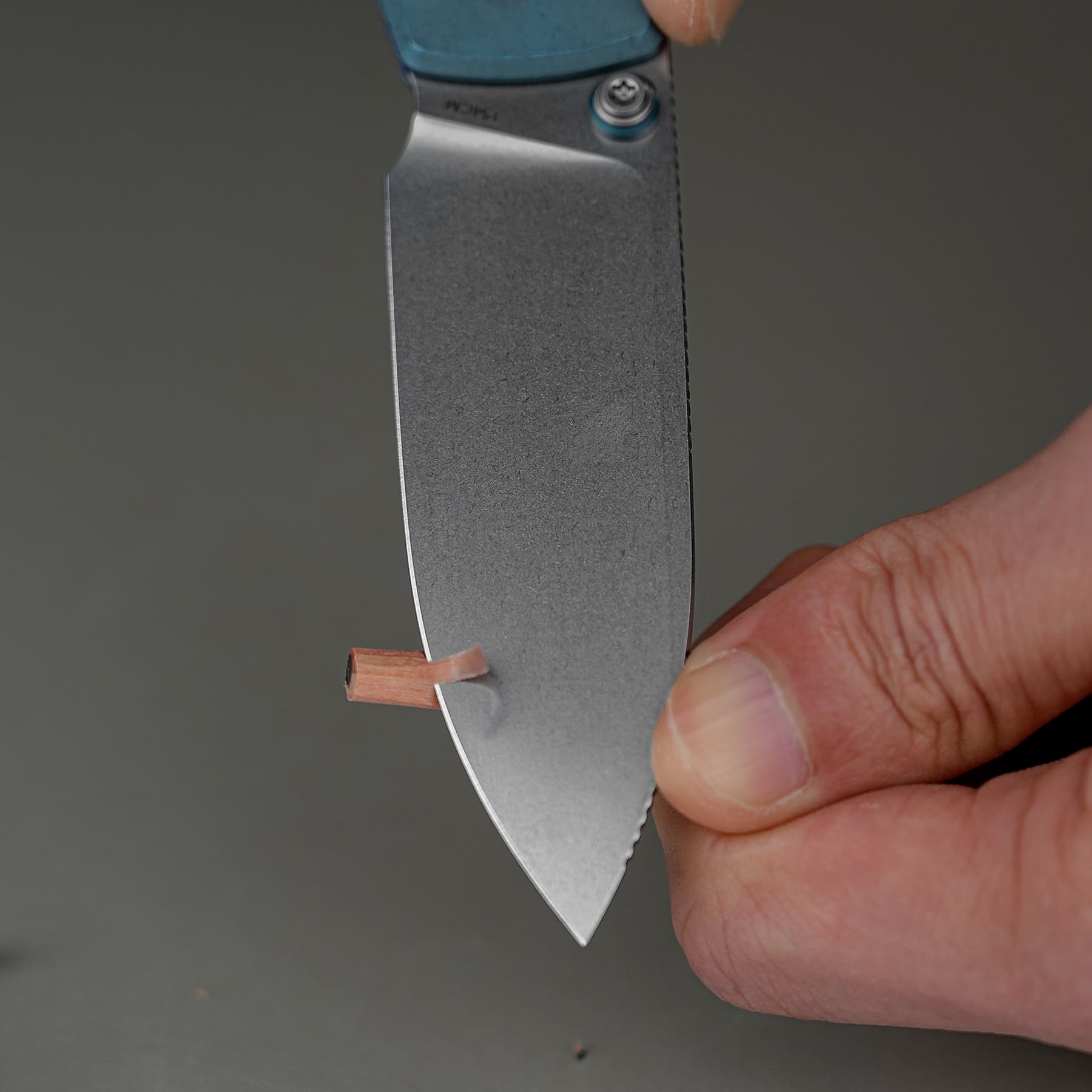 Close-up of a handheld knife blade with a small copper shim near the edge as fingers guide it