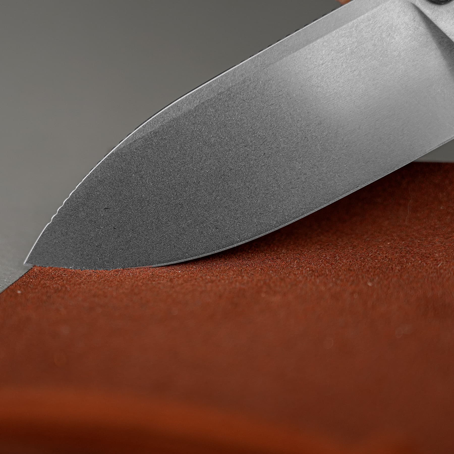 Close-up of a large kitchen knife blade resting on a reddish-brown cutting surface, edge visible and sharp.