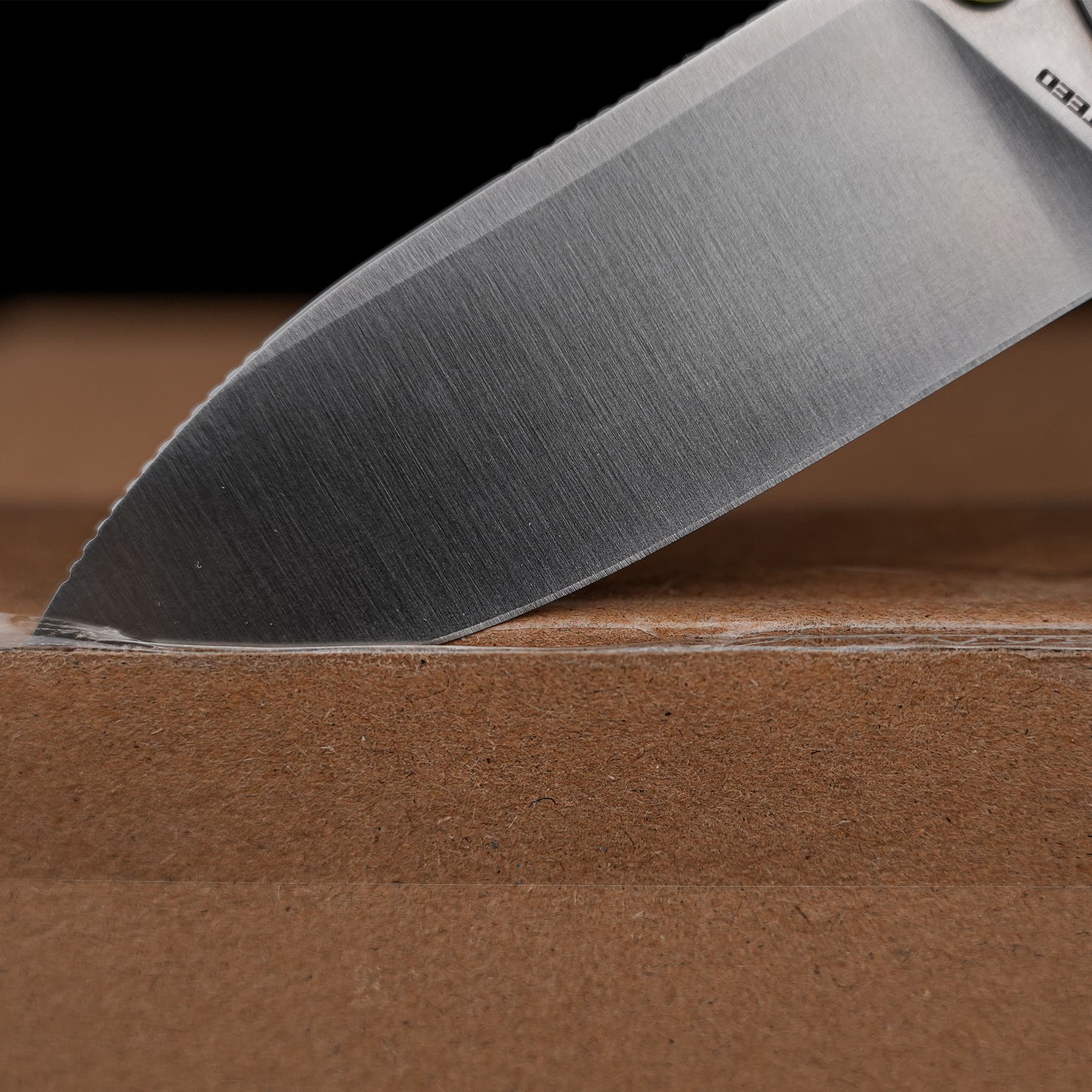 Close-up of a sharp stainless knife blade angled as it cuts into a wooden cutting board