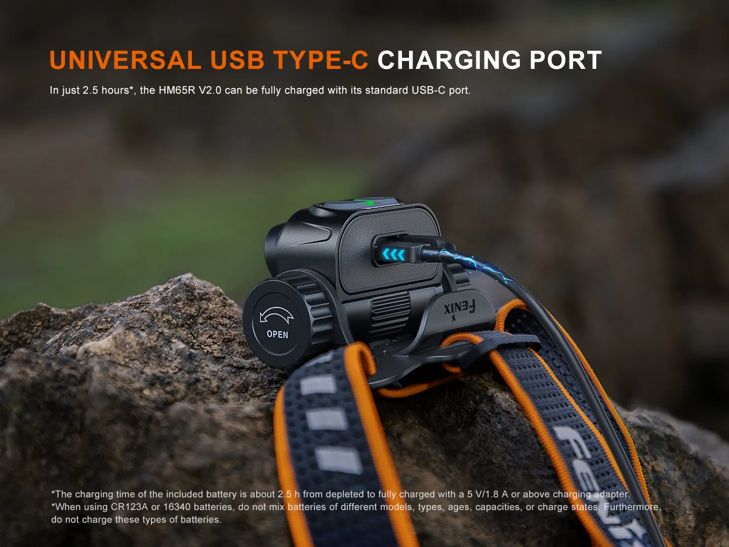 Close-up of a rugged black headlamp battery with a USB-C cable plugged in on a rocky surface, orange strap visible.